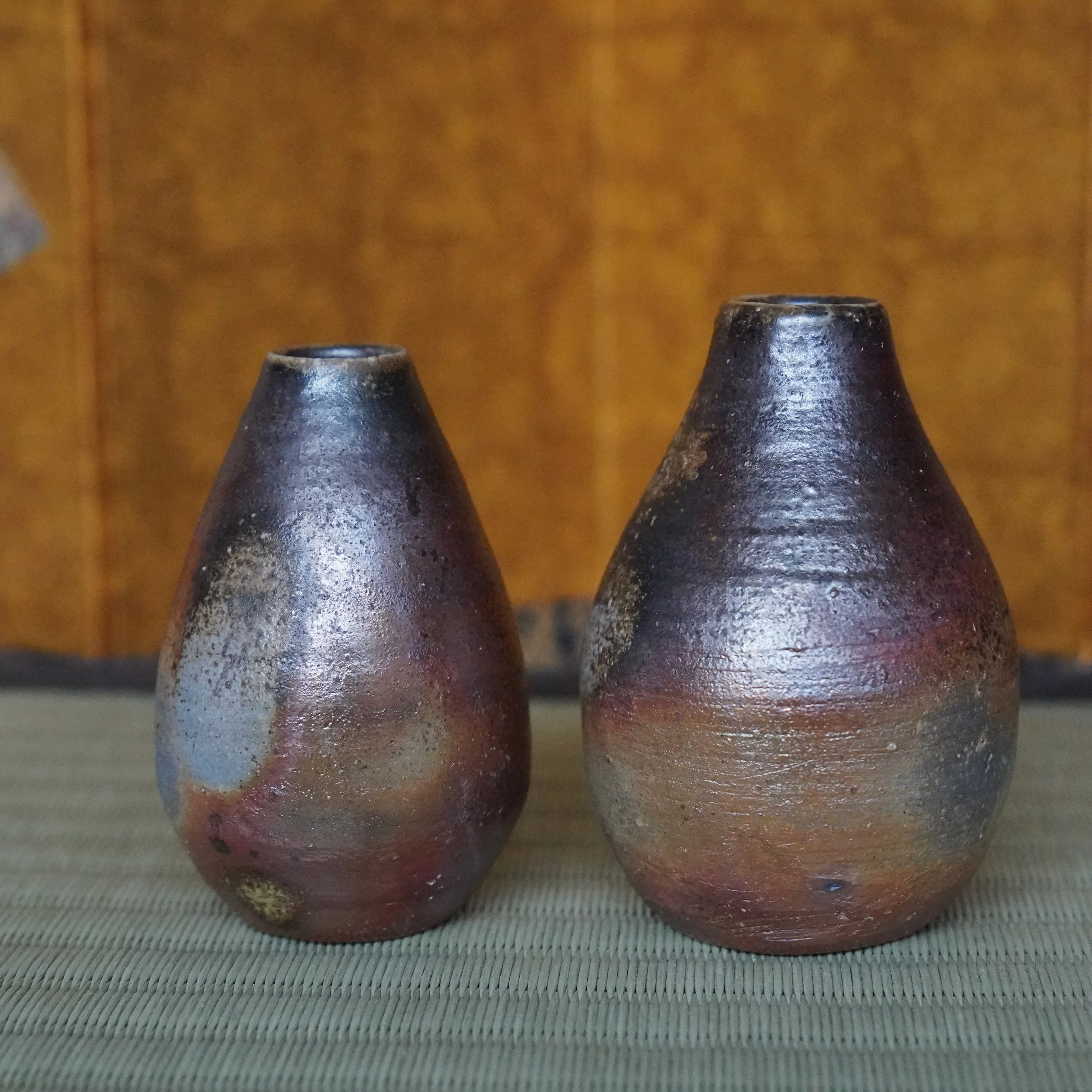 Bizen-yaki tokkuri vases by Shibaoka Tōsendō. Two teardrop-shaped pieces, one aubergine with silvery shimmer, the other rustic orange, on a tatami.