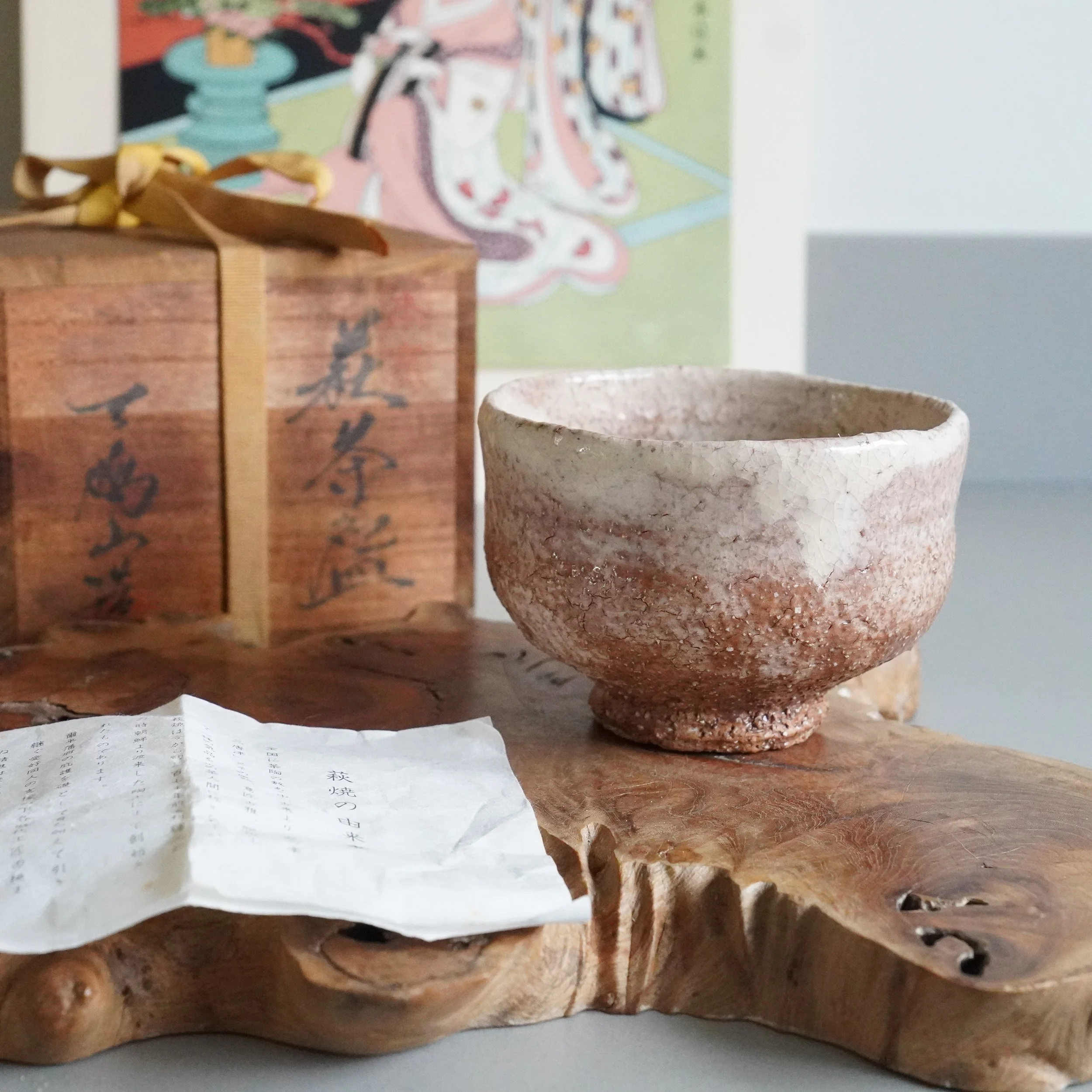 Oni-Hagi-yaki chawan Hirose Nanshū founder Tenpōzan kiln rough textured surface on wooden plank with tomobako and shiori, ukiyoe print in background,early Shōwa era Japan