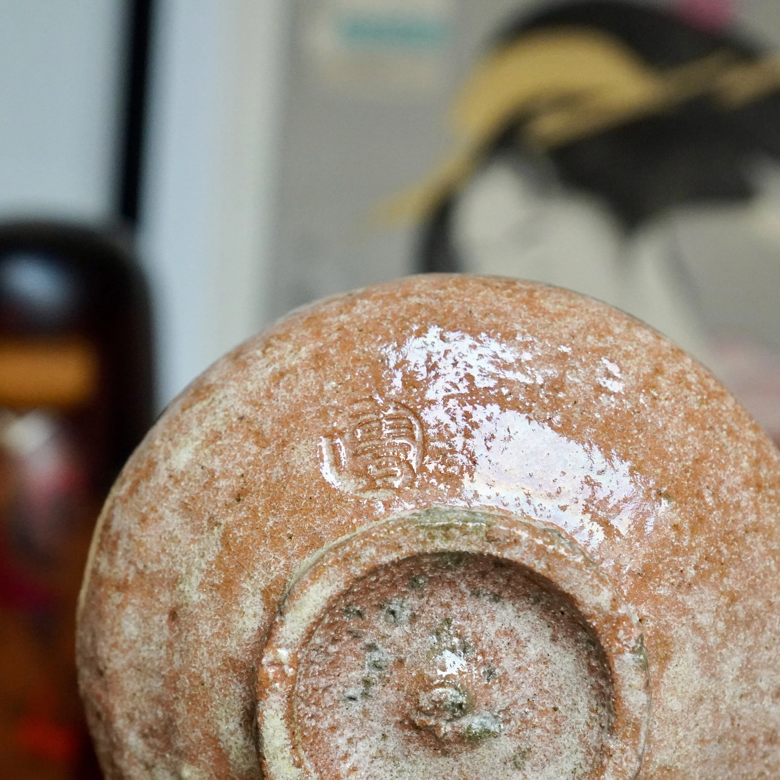 Underside of an aka-raku chawan by Sawada Hiroyuki, showcasing its reddish-brown, rugged surface with glossy white glaze pooling and an impressed signature.