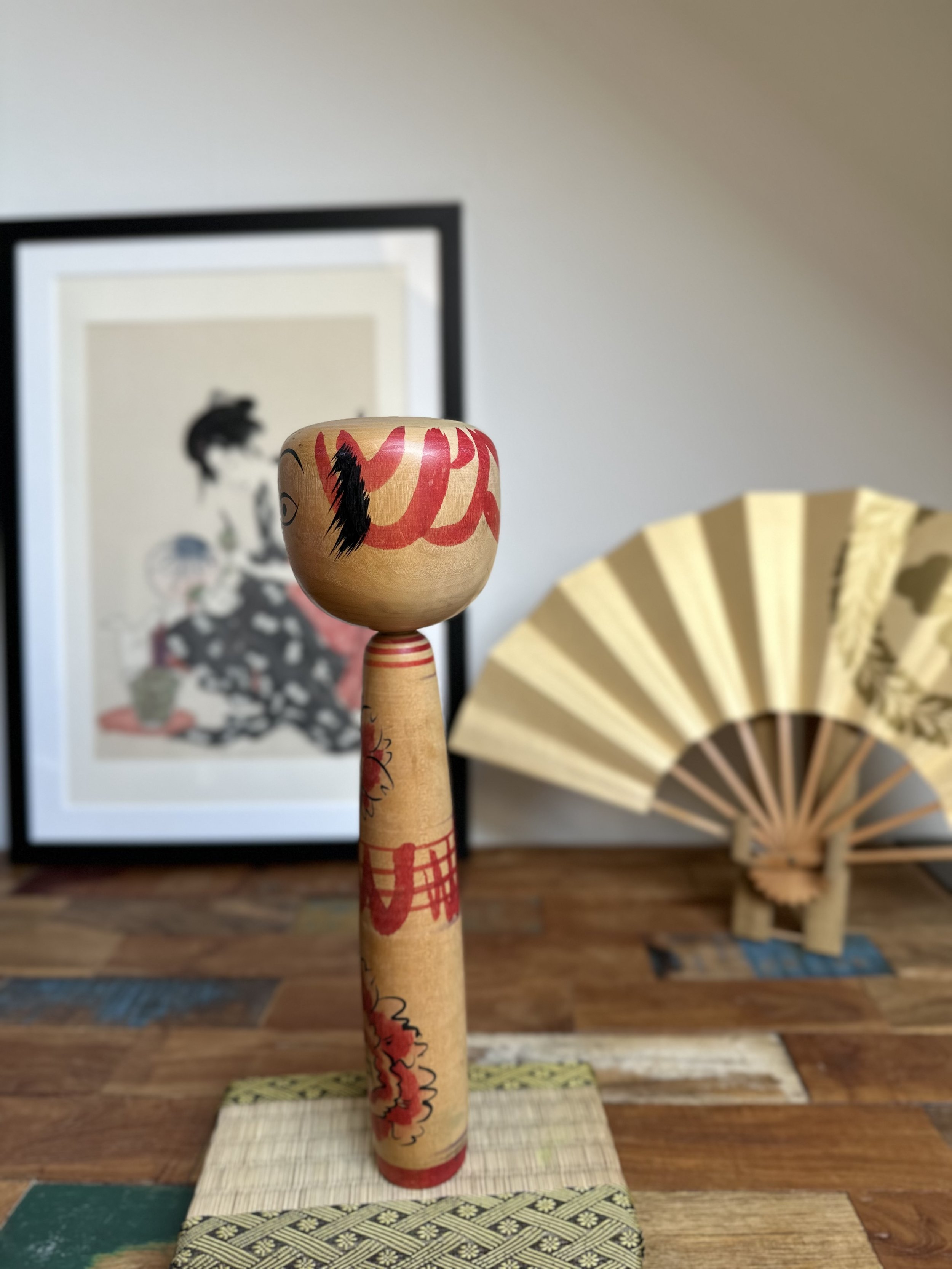 Seya Jūji Nakanosawa Takobozu kokeshi with a large head and tapering body, decorated with red brush strokes, black hair, and cherry blossom patterns.