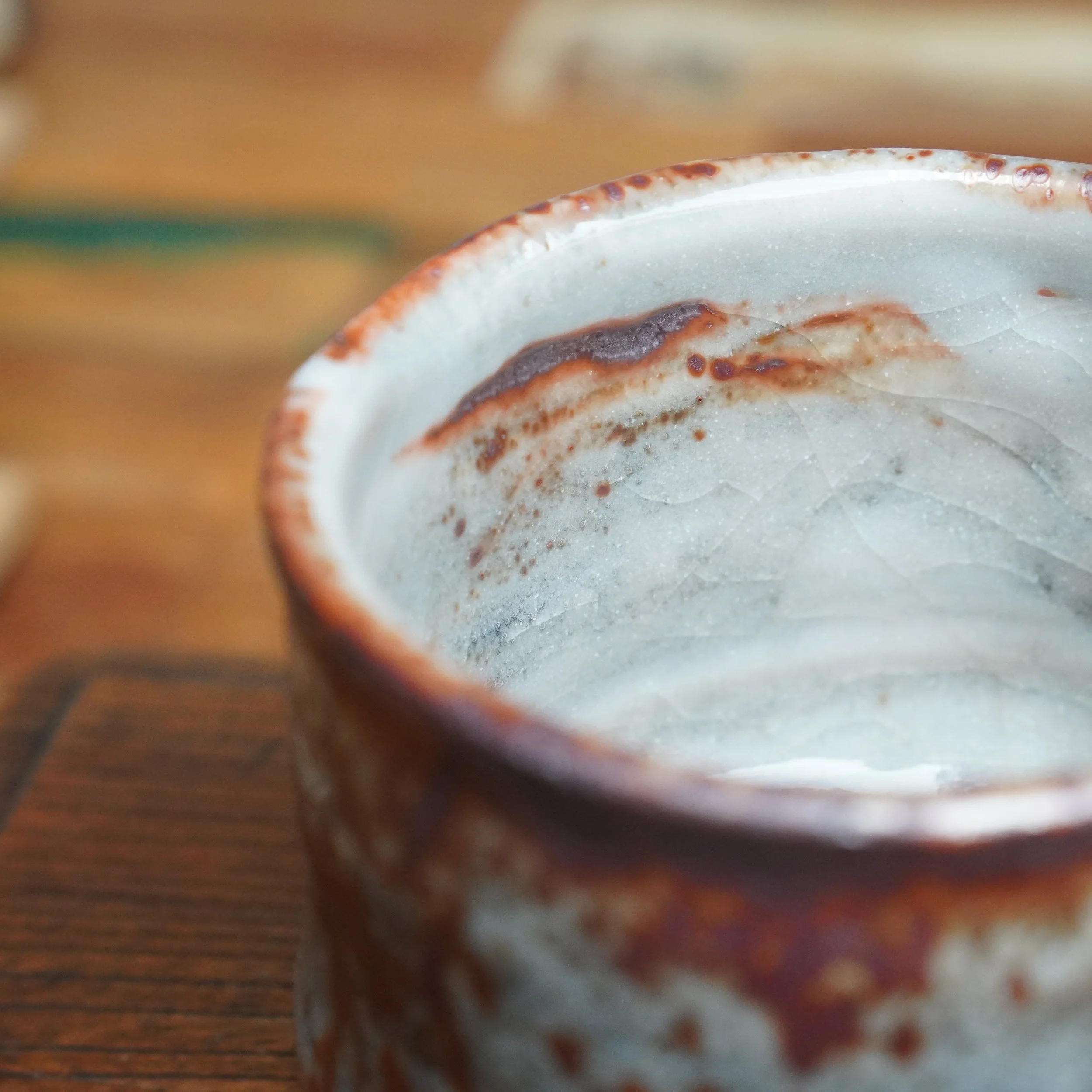 Close-up of a chawan's interior and rim, featuring a pale grey crackled glaze with mottled red-brown speckles and patches.