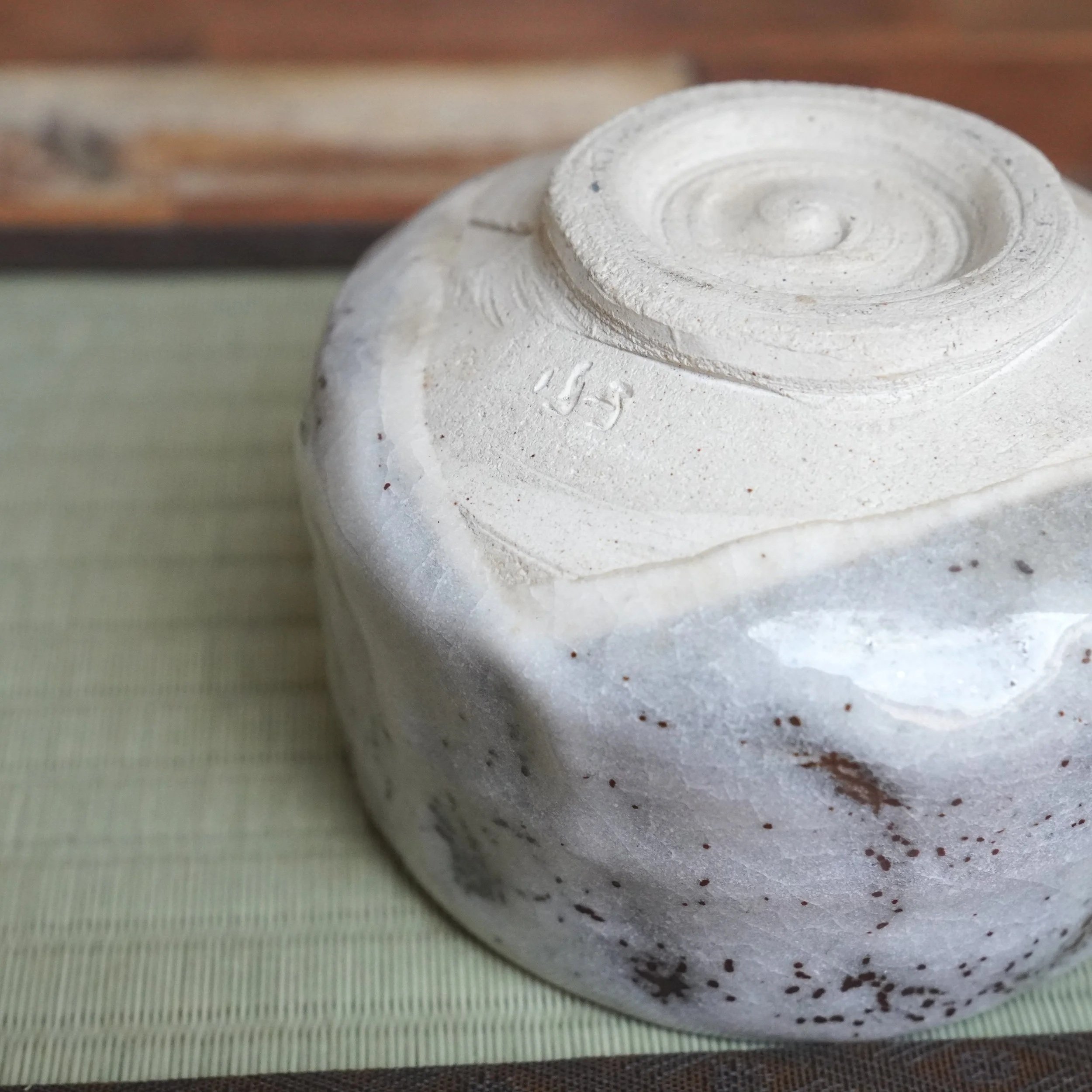 Underside of a chawan by Shōzan, featuring textured off-white glaze, rust-brown speckles, and indented sides. A spiral mark and '正山' signature are on the base.