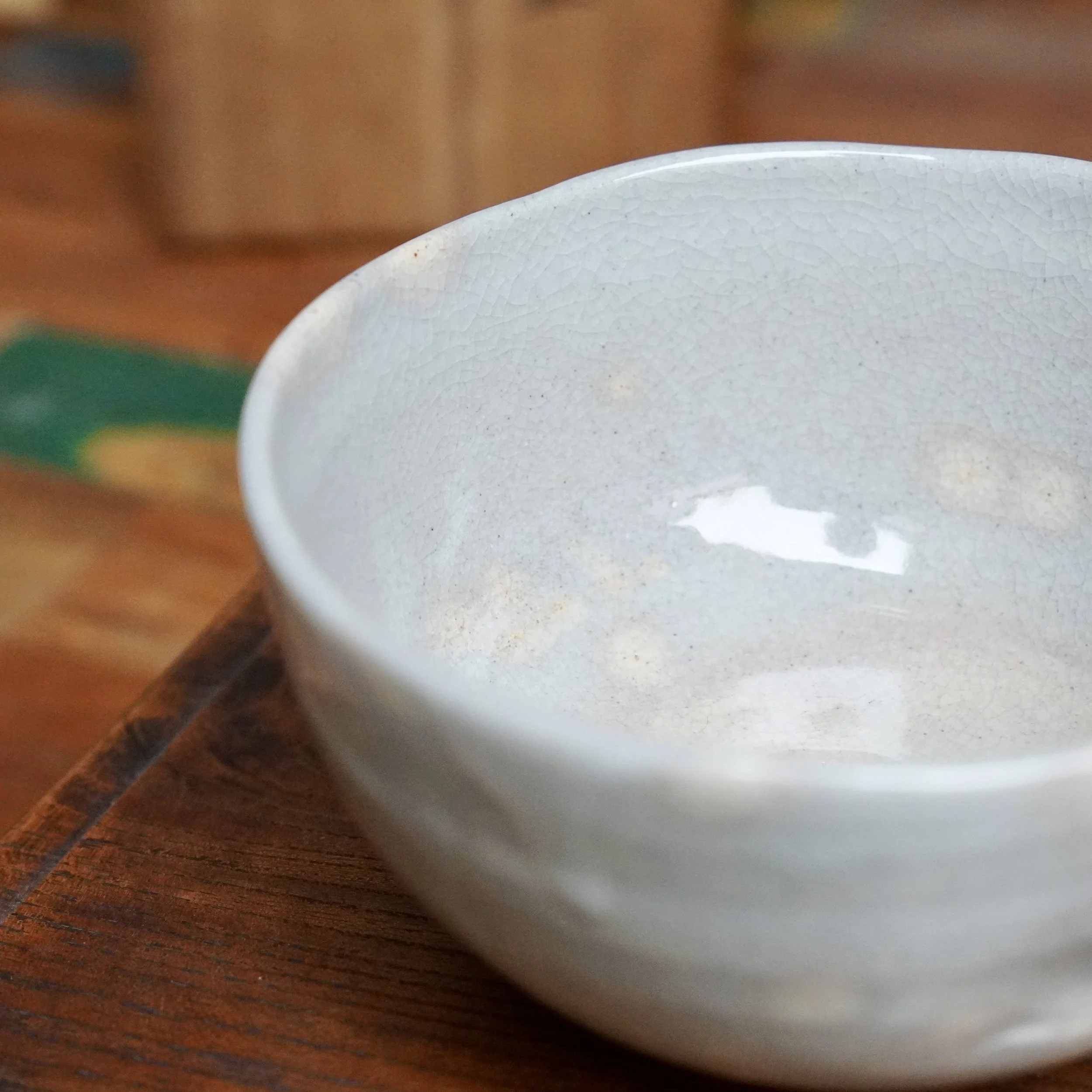 Close-up, angled view of a ceramic chawan by Nagasawa Minoru. It has a soft grey-blue crackled glaze with hints of pink blush.