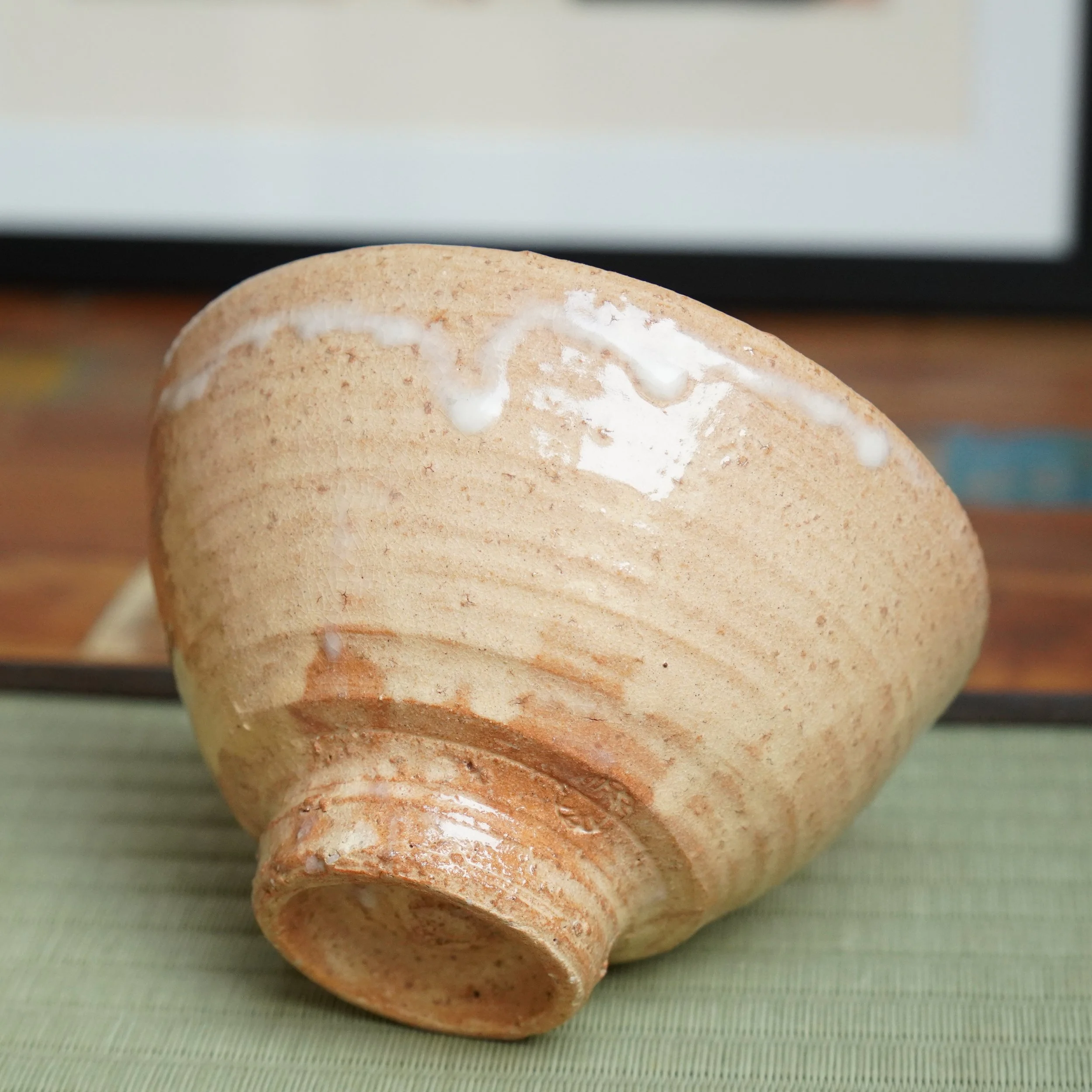 Hagi-yaki chawan by Kaneko Nobuhiko, angled on its side, showing white glaze drips on a wheel-marked, speckled beige and reddish clay body.
