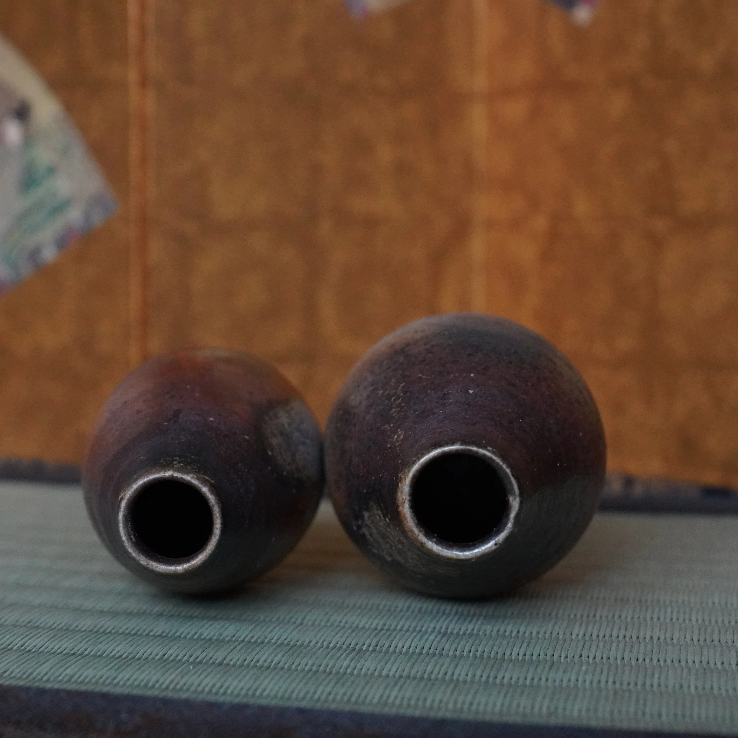 Pair of Bizen-yaki tokkuri vases by Shibaoka Tōsendō, Kōzan-gama. Dark, textured spherical forms with narrow openings, showing aubergine, silvery-blue, and rust tones on a green tatami mat.