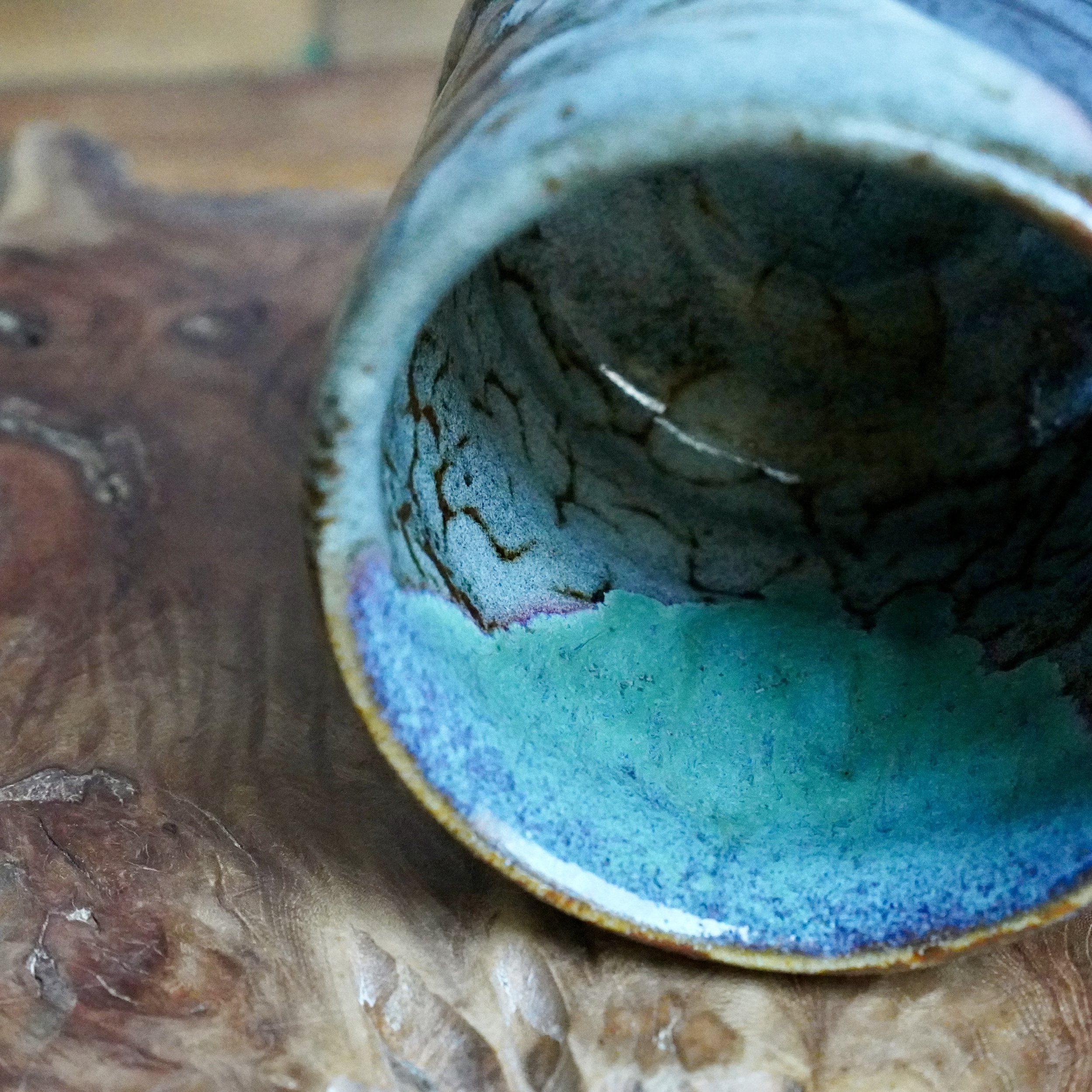 Close-up of a ceramic tsutsu chawan interior, featuring vibrant turquoise glaze, transitioning to speckled grey with brown crackle lines and an iridescent rim.