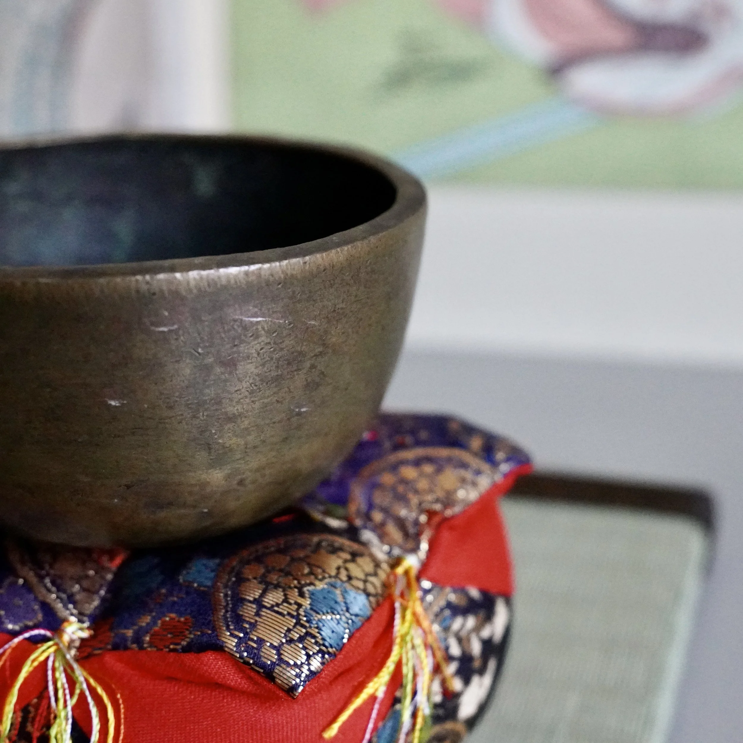Small bronze orin singing bowl with striker resting on brocade cushion, front view