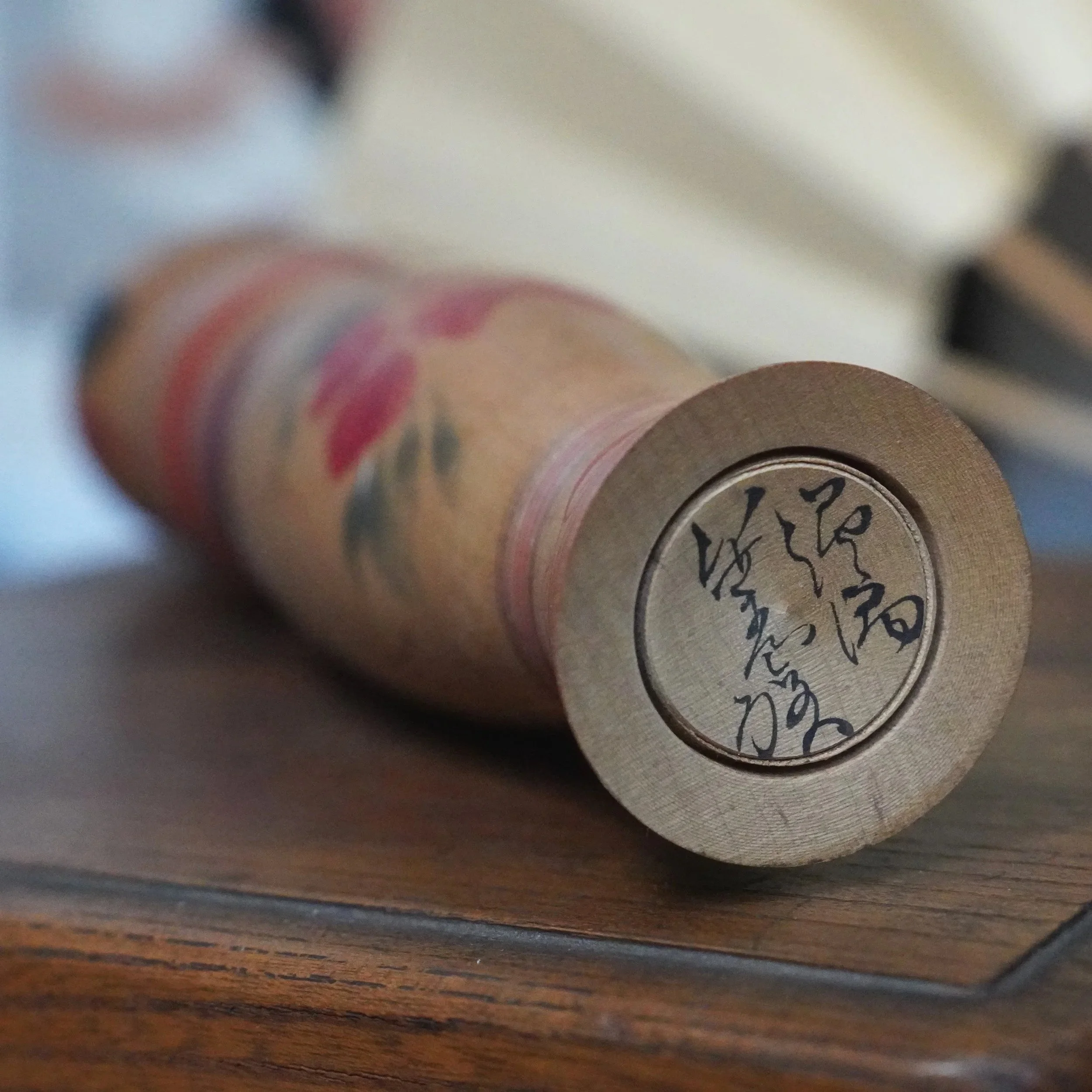 Wooden kokeshi doll, side view, with a red and purple peony motif and Sasamori Junichi's black ink signature on the base.