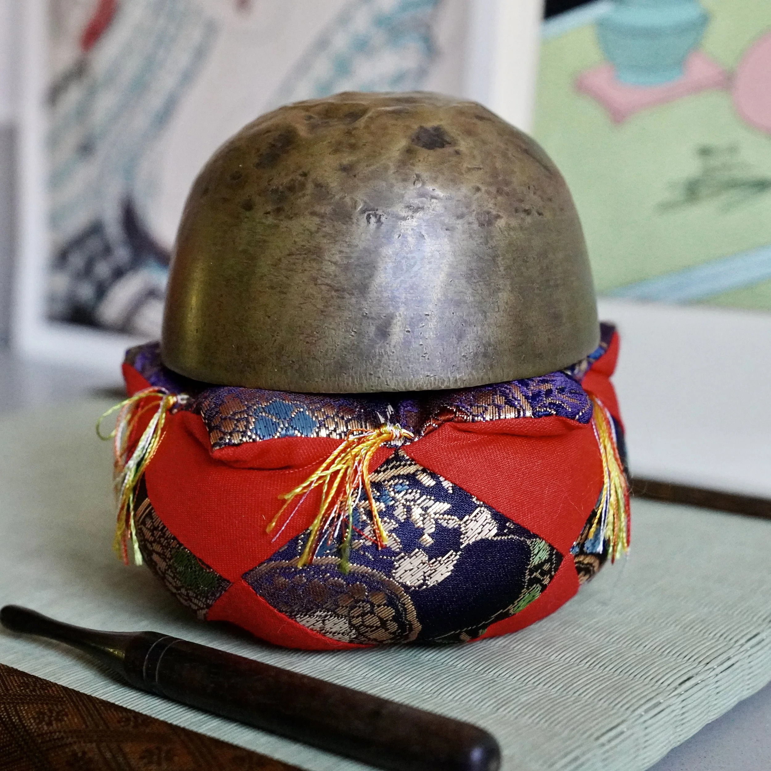 Underside of small bronze orin singing bowl showing rounded hammered surface, brocade cushion
