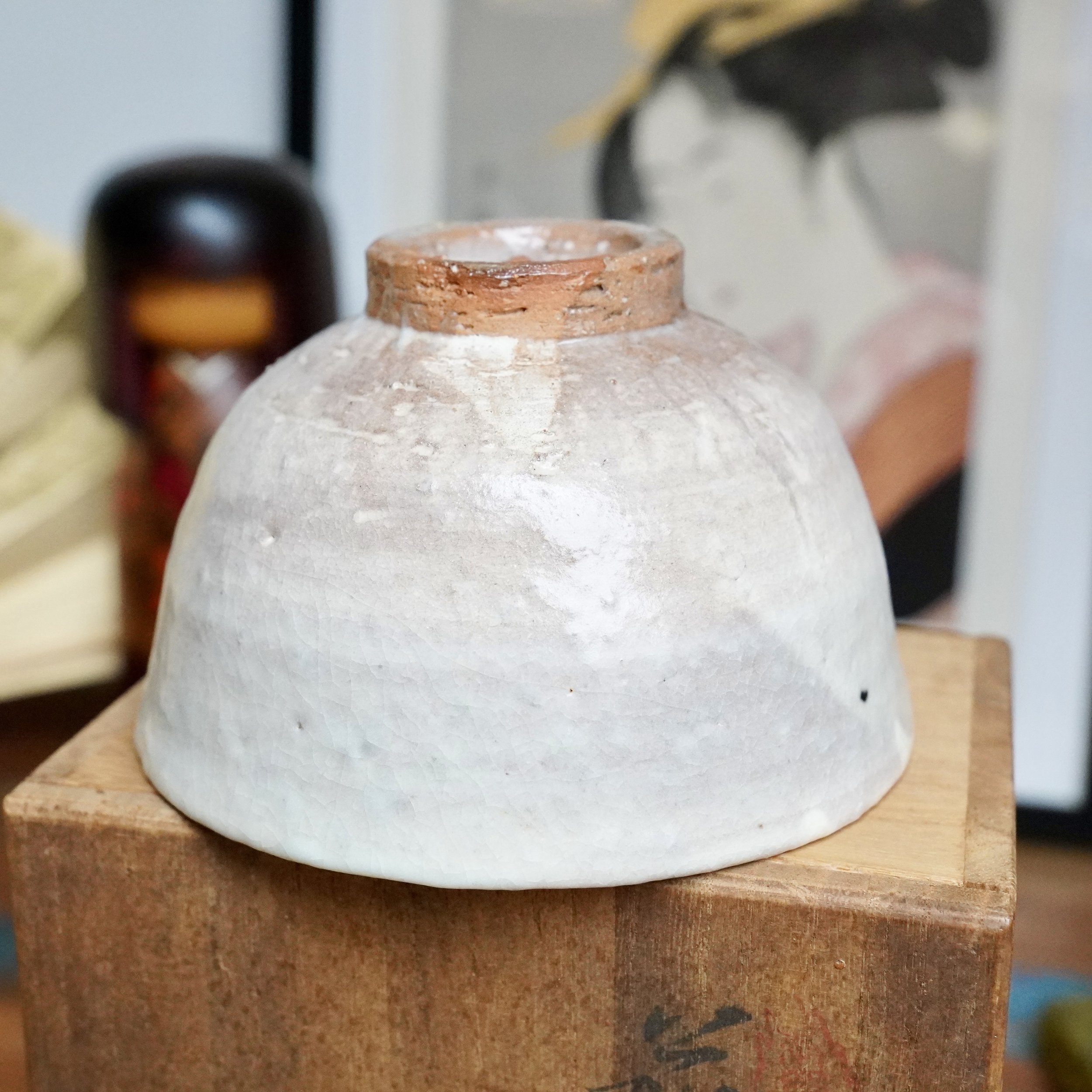 Tamamura Shōgetsu Hagi-yaki chawan, inverted, with a reddish-brown bare clay foot and white crackled glaze, on a wooden box.