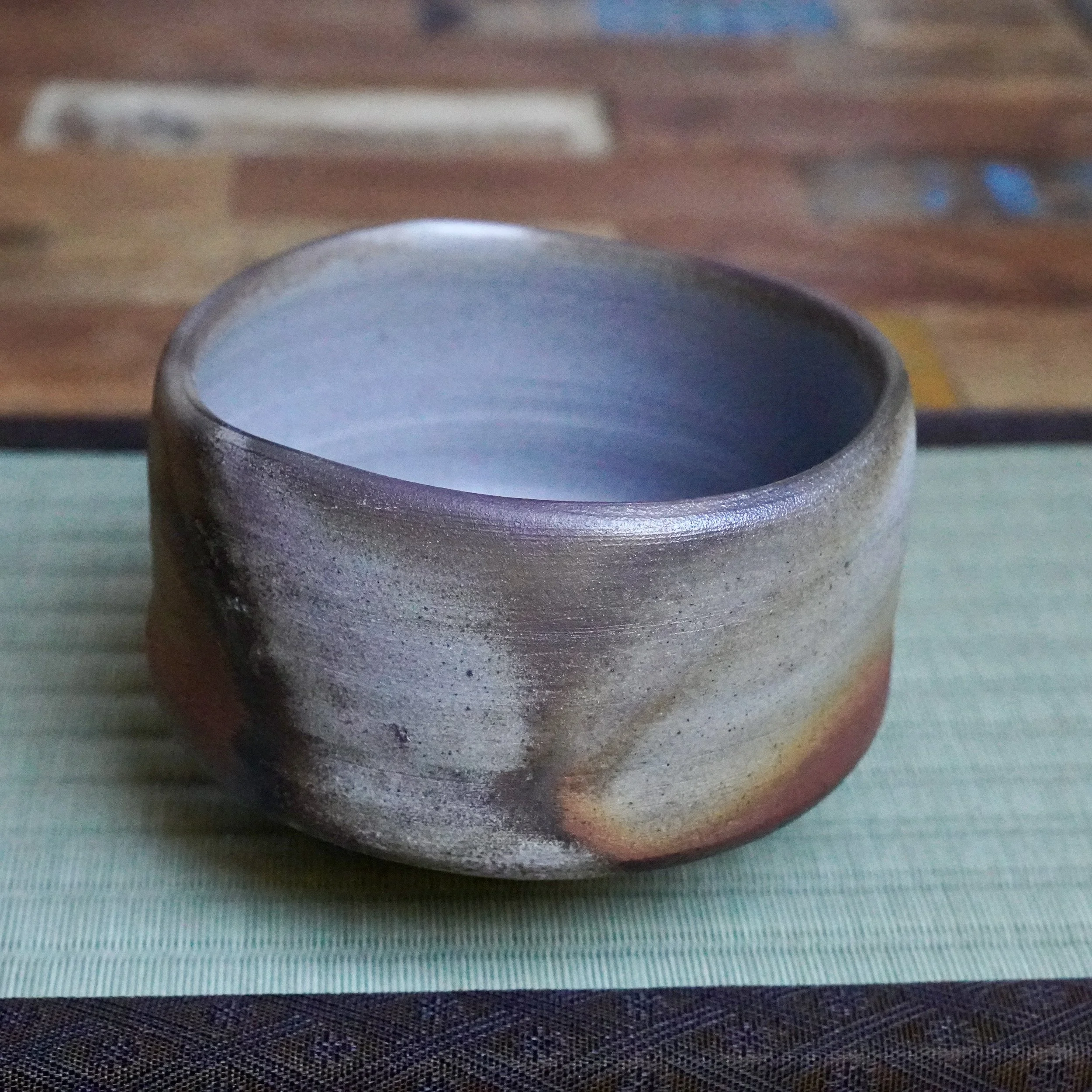 Inomata Masaaki's Sangiri Bizen chawan, with an unglazed grey exterior showing fiery rust and burnt orange markings, a silver-dusted rim, and light blue interior.