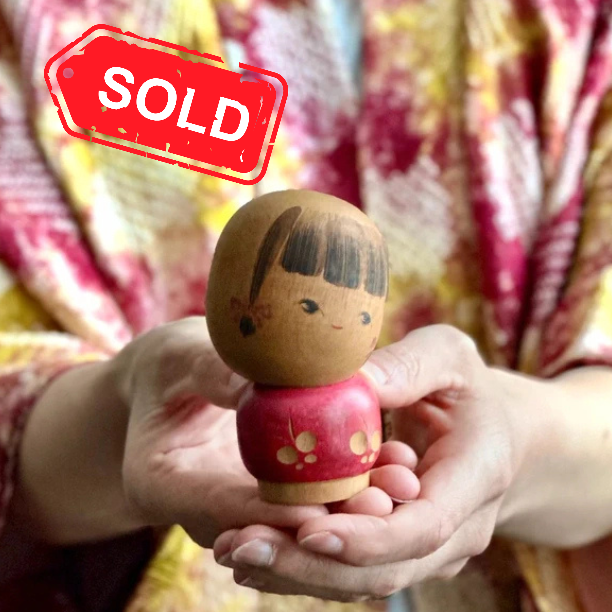 Small sōsaku kokeshi signed by Sato Suigai, Shōwa period held in hands by woman wearing haori jacket