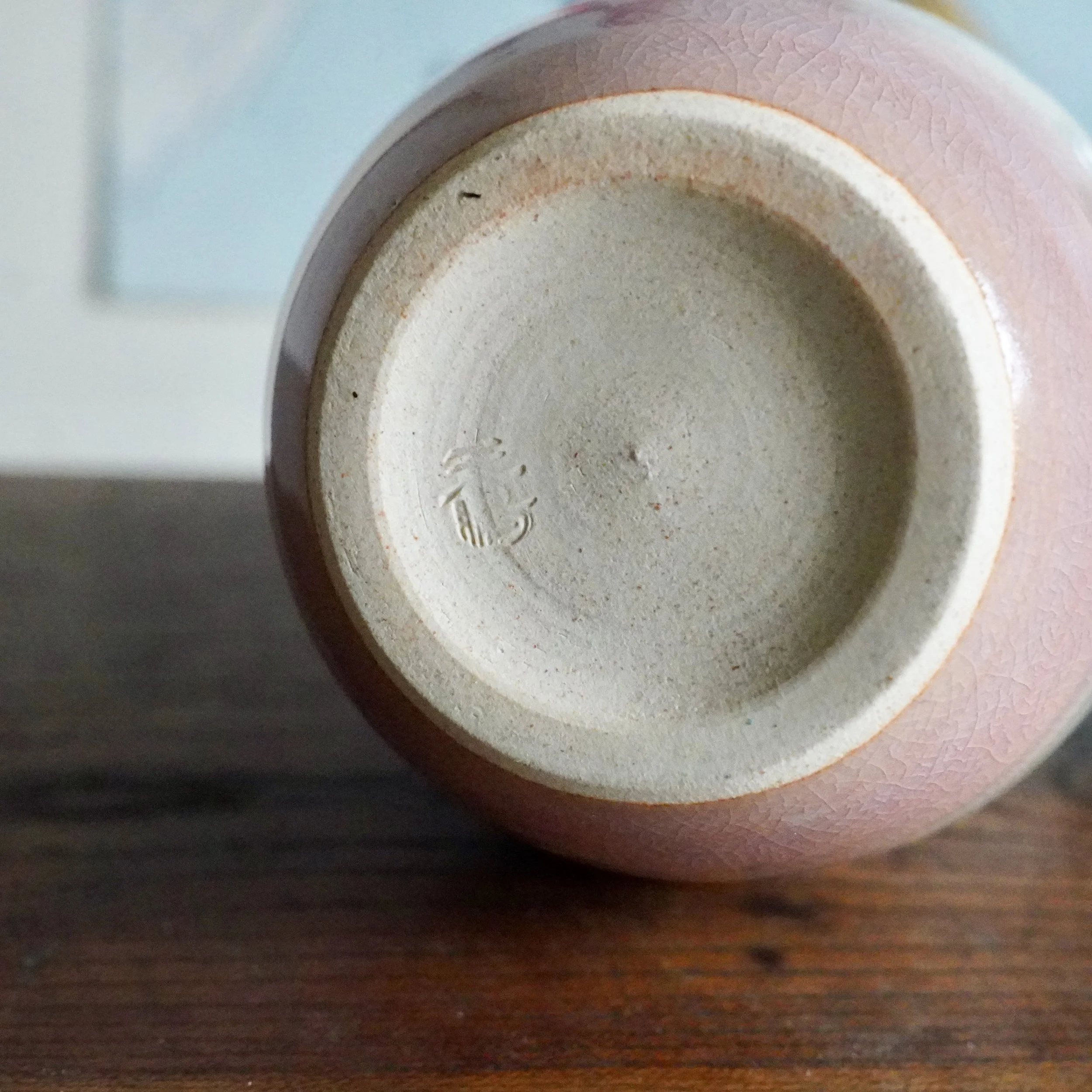 Underside of a pink Hagi-yaki sake vessel, revealing an unglazed foot with a kiln stamp and a crackled glaze surface.