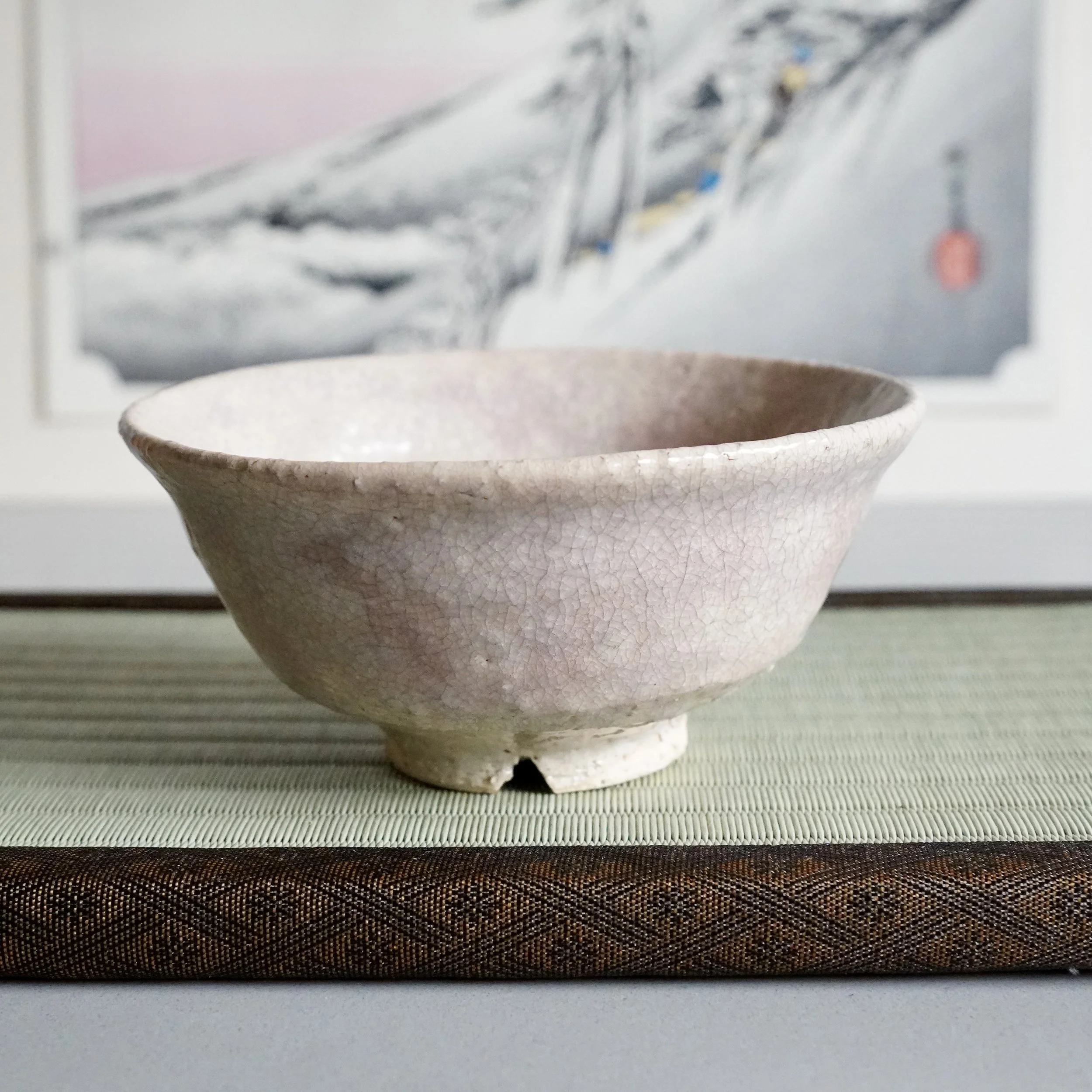 Japanese matcha bowl front view on kirikōdai foot, Hagi-yaki crackled glaze, ukiyoe print behind