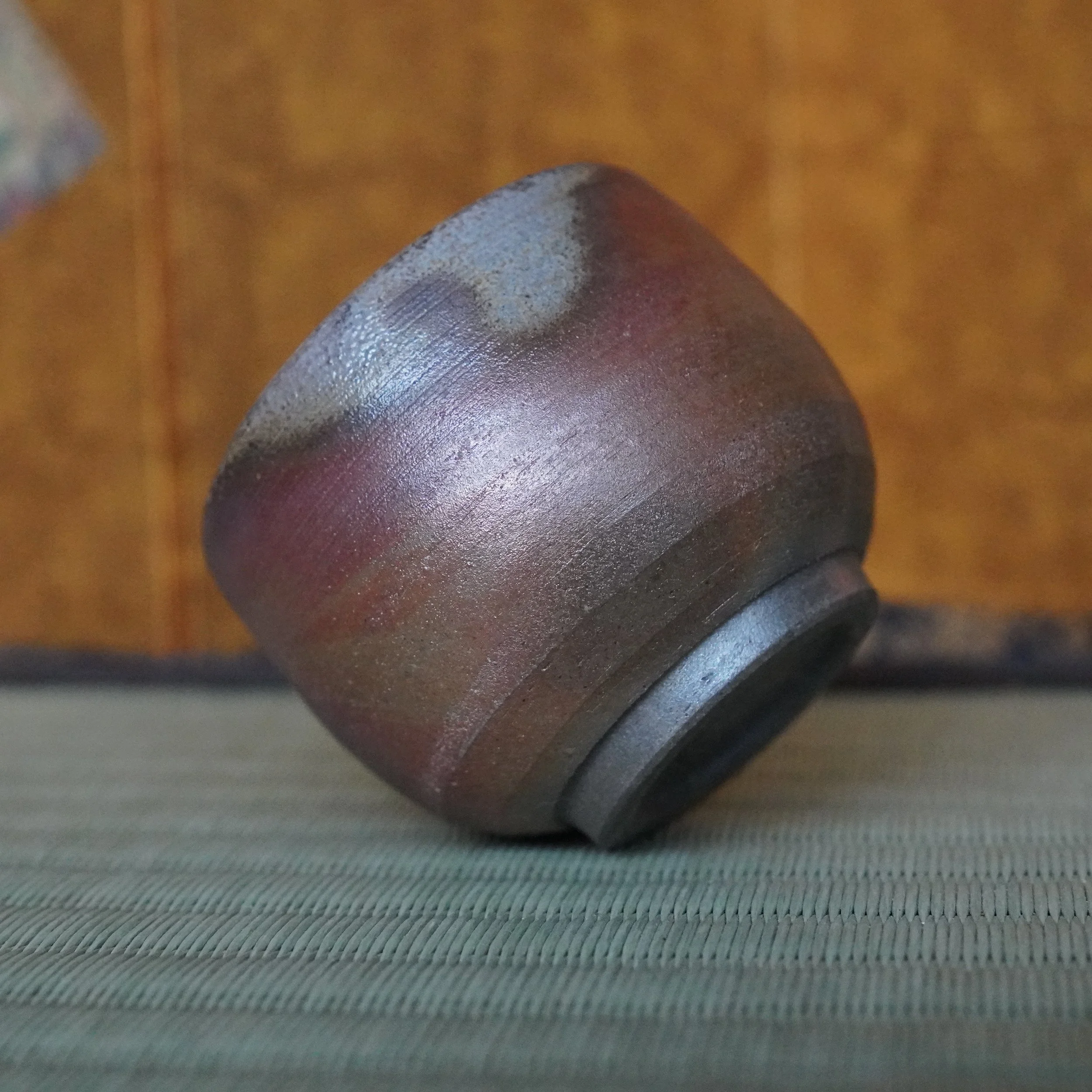 Bizen-yaki guinomi by Yamamoto Sōshū, featuring reddish-brown hidasuki flame marks and a textured surface, tilted on a tatami mat.
