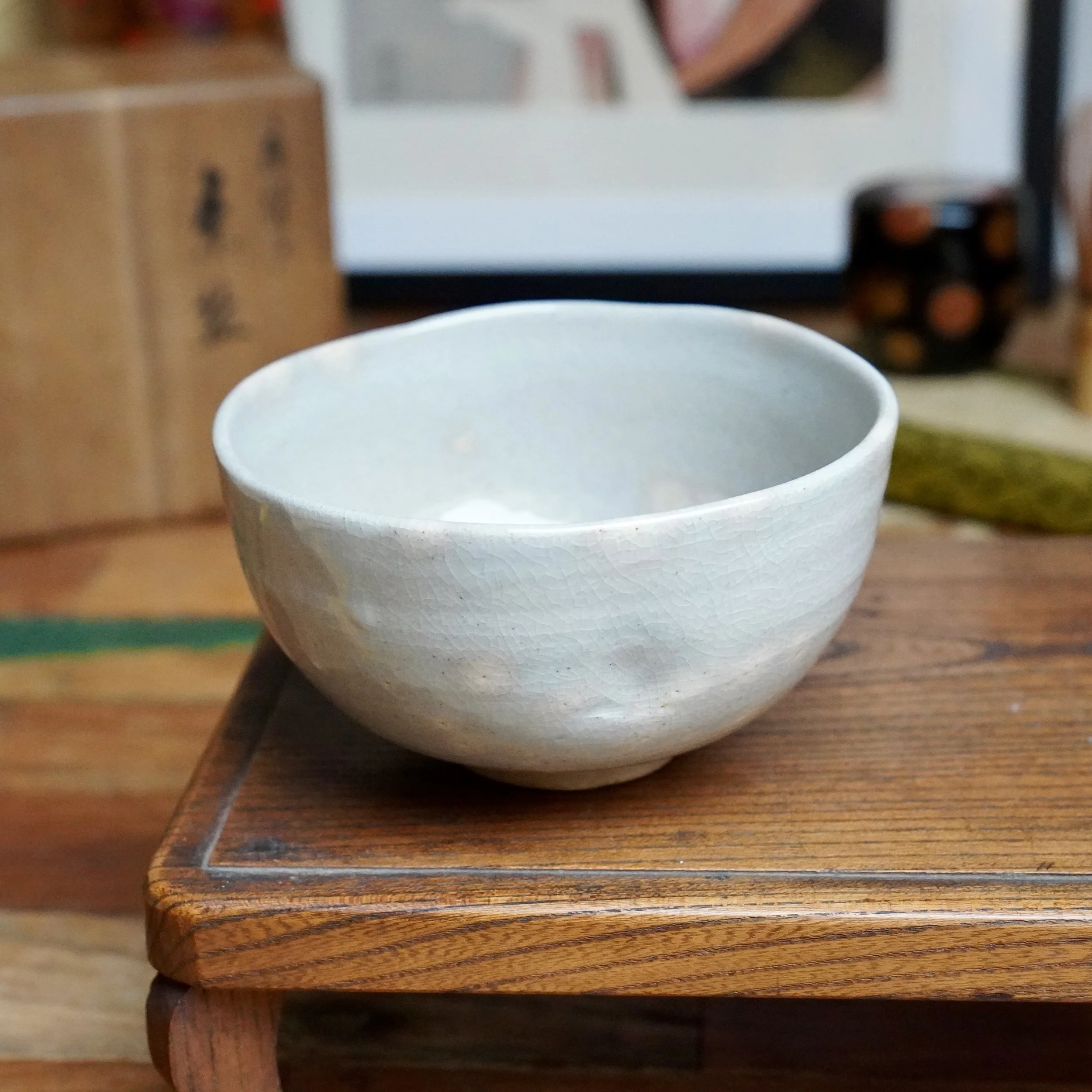 Izushi ware chawan by Nagasawa Minoru, a grey-blue crackled ceramic bowl with a subtly flattened rim, showing a pink blush, resting on a wooden stand.