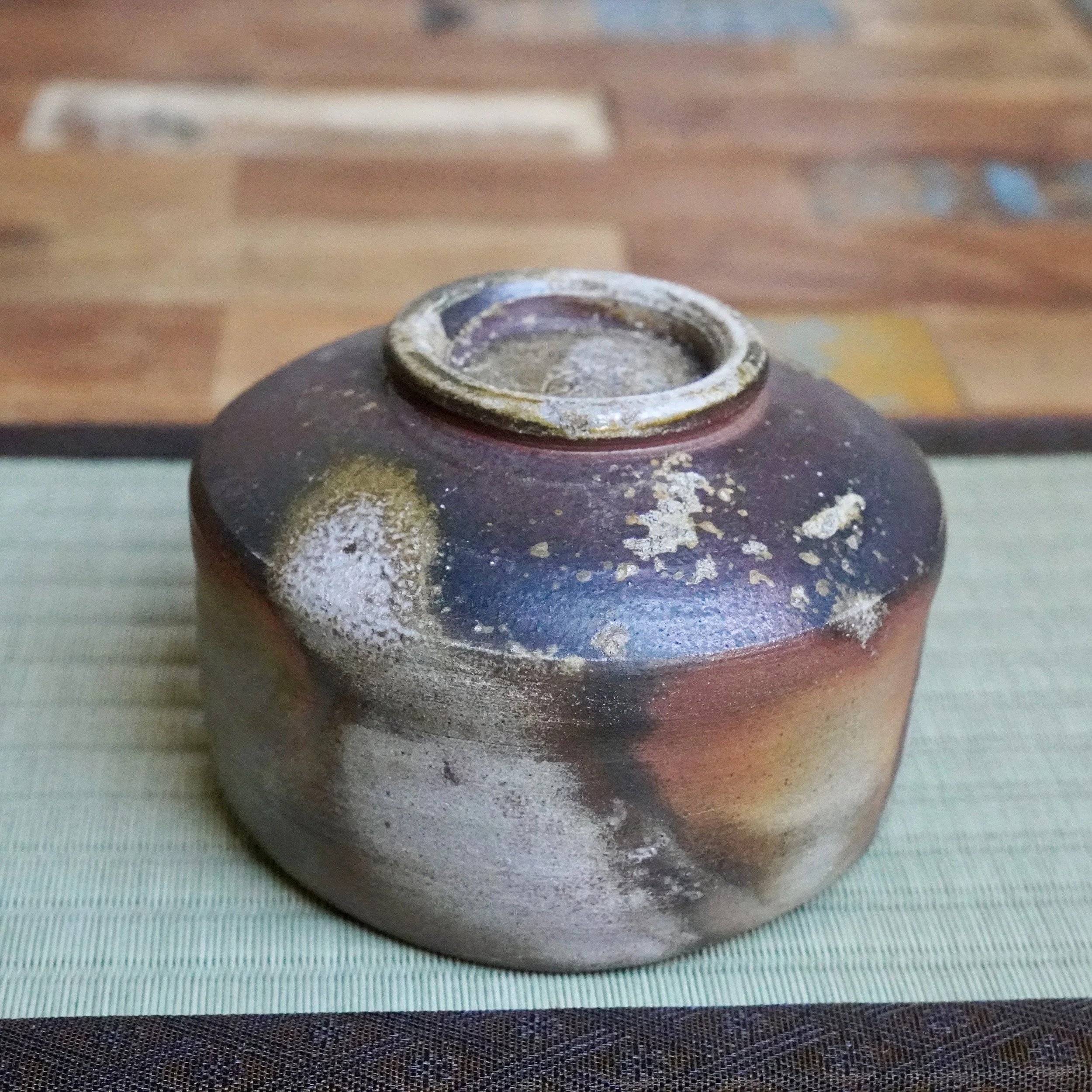 Inomata Masaaki Bizen chawan showing deep rust and purple-grey firing marks, with an ash-dusted rim, on a green tatami mat.