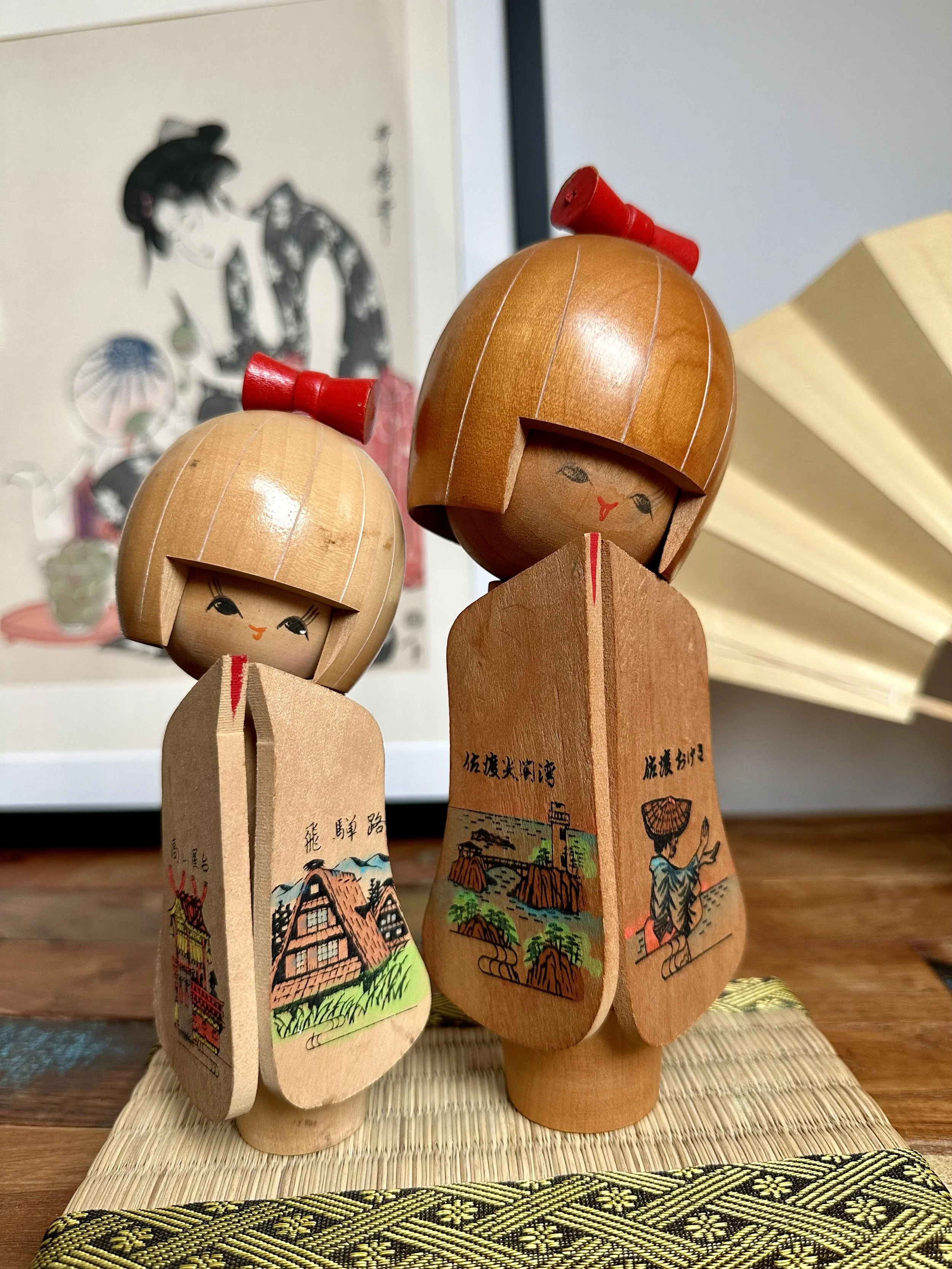 Three-quarter view omiyage kokeshi pair panels open Sado Hida region ukiyo-e print backdrop