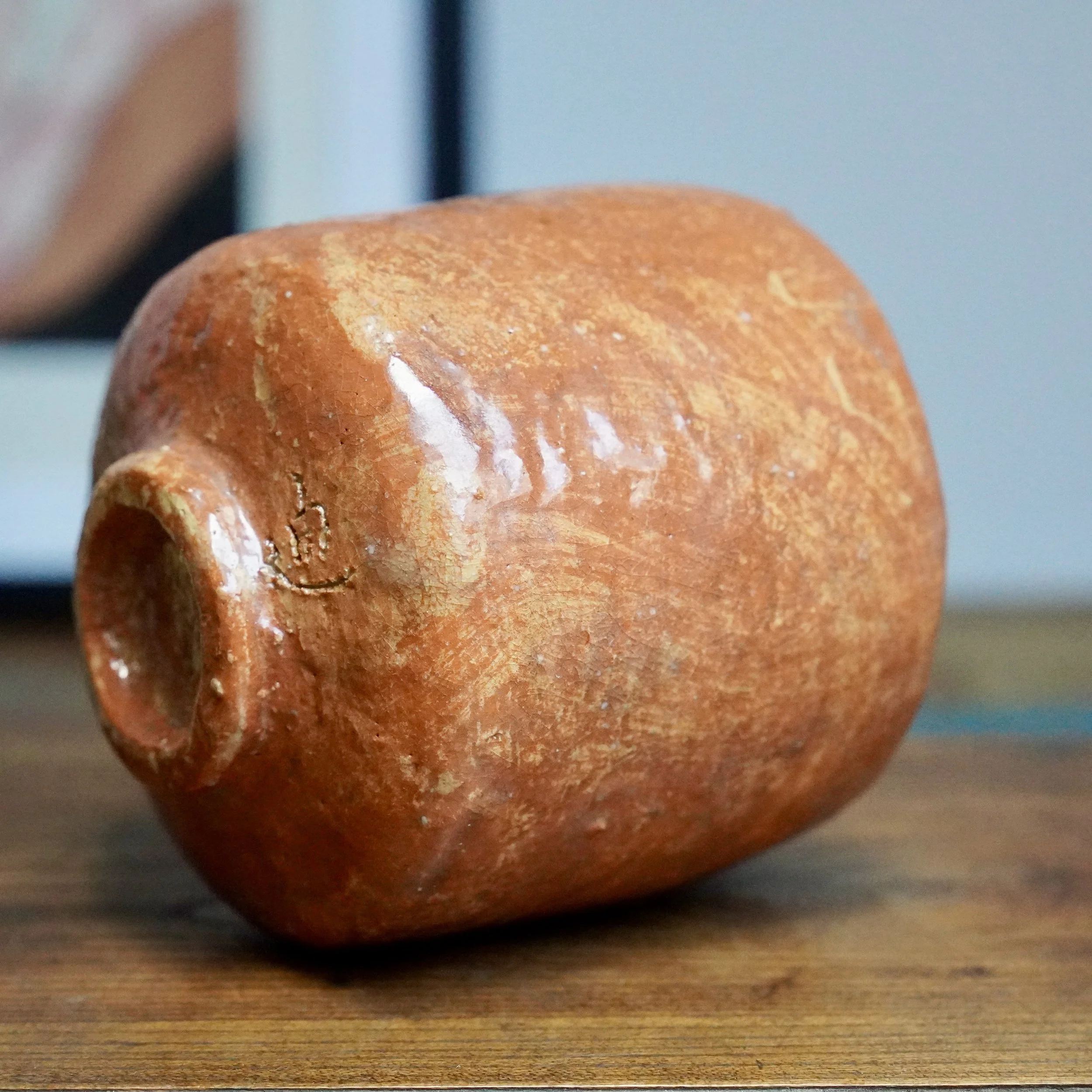 Terracotta-colored tsutsu shape bowl lying on its side, revealing a footrim and an impressed mark. Its surface features cream-colored streaks and textured glaze.