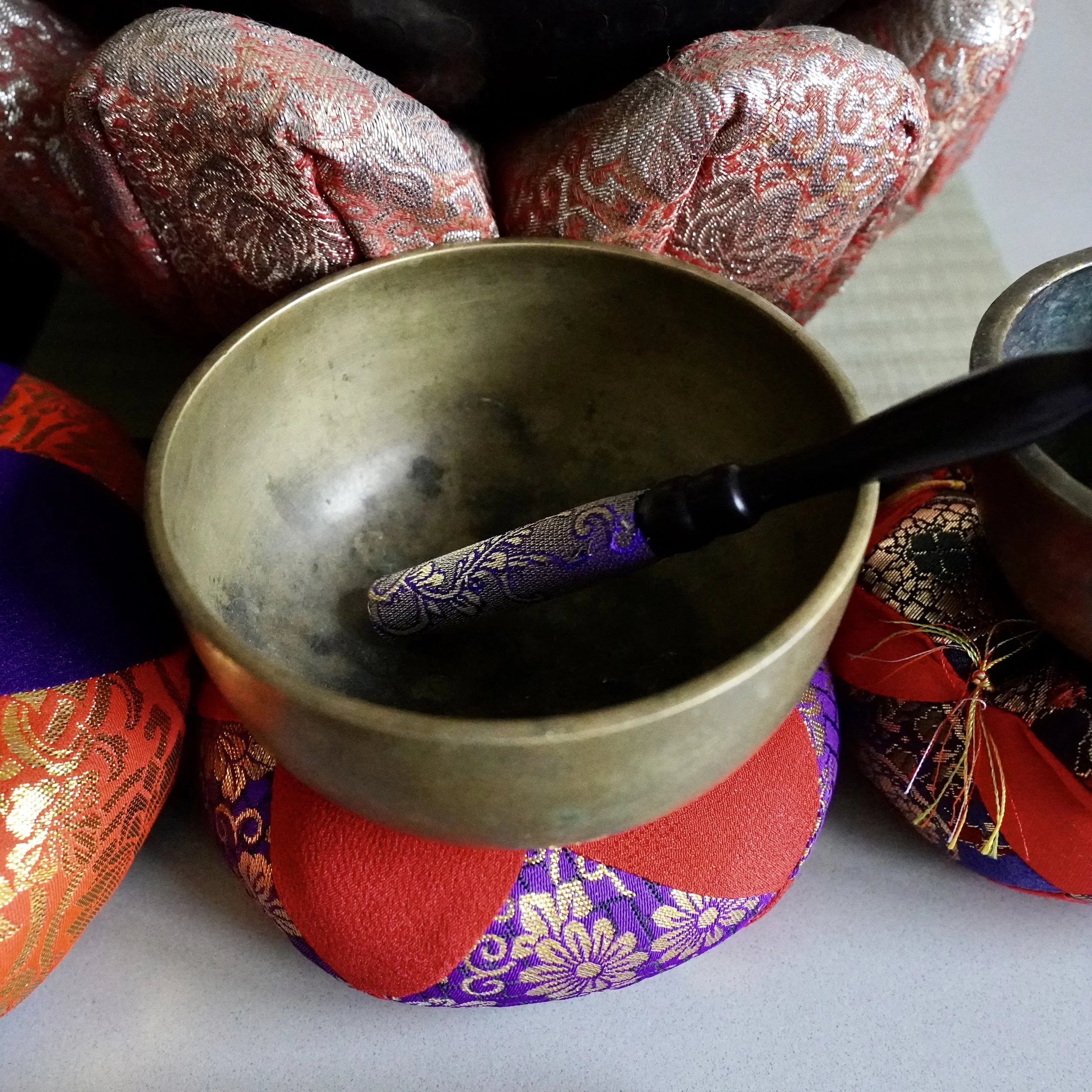 Bronze orin singing bowl with striker among red and purple brocade cushions, styled group setting
