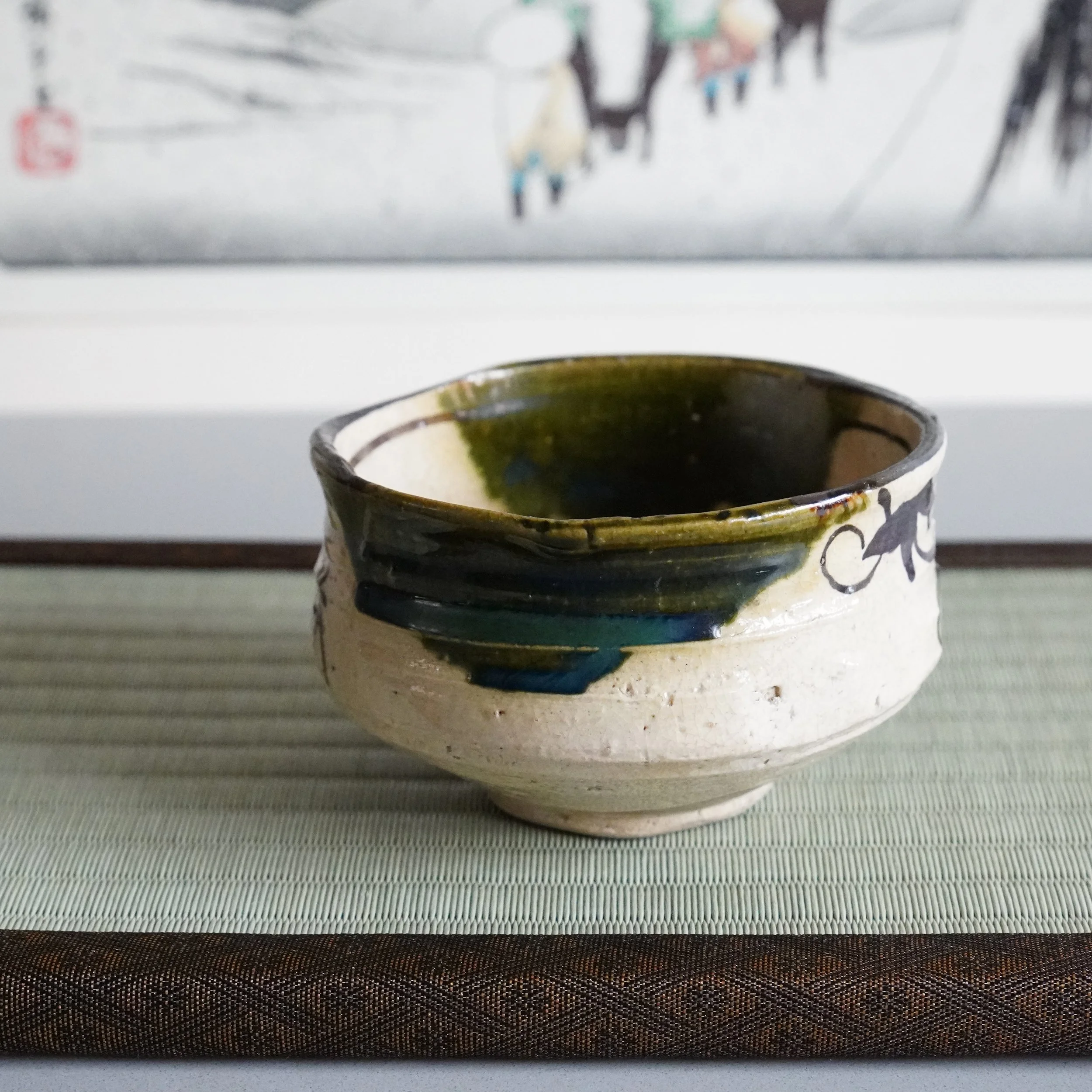 Ao-Oribe matcha bowl three-quarter angle iron brushwork figures and green glaze dripping over rim cream stoneware Mino ware Gifu Prefecture vintage Japanese chawan