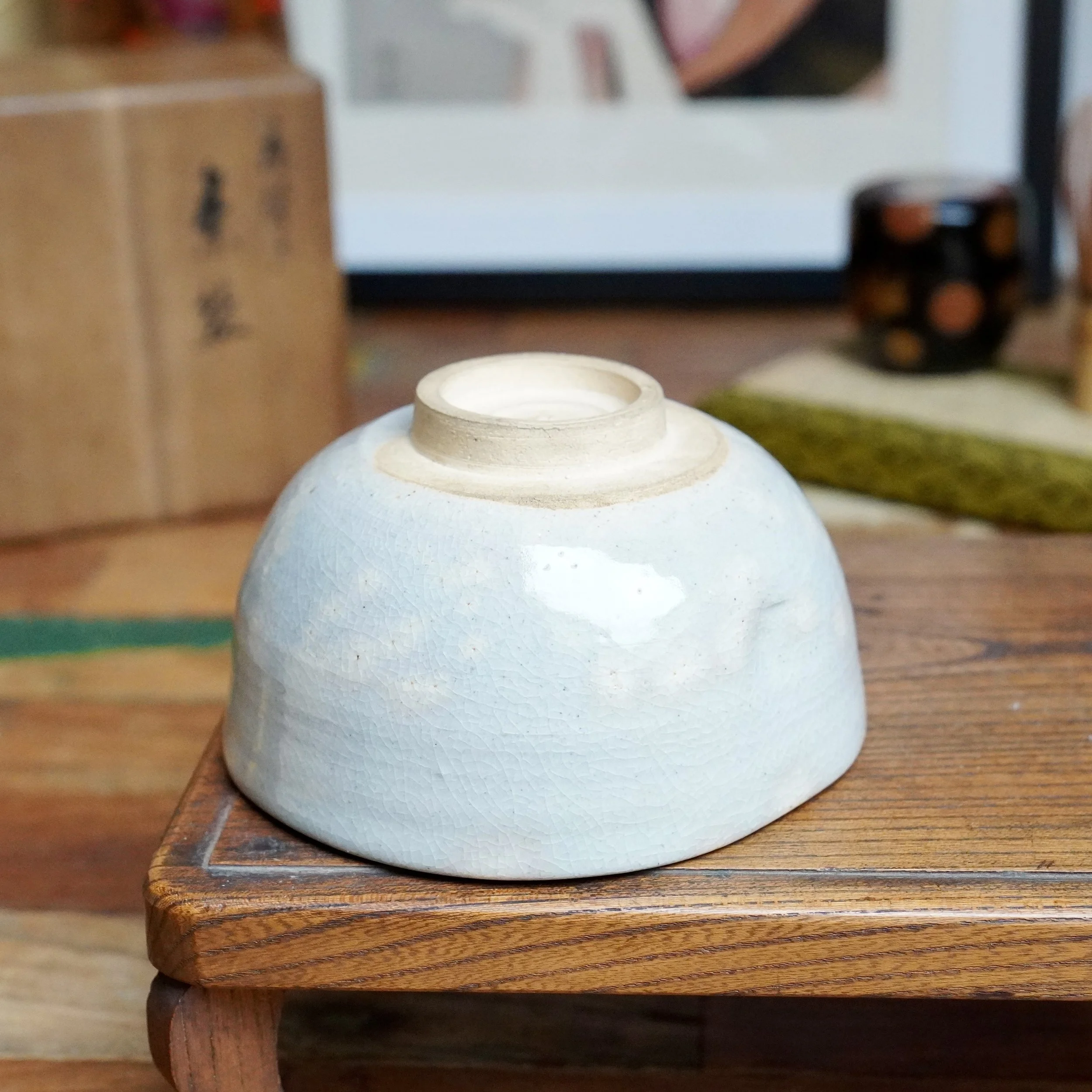 Underside of Nagasawa Minoru chawan by Izushi-gama, displaying a light blue crackled glaze and unglazed footrim on a wooden surface.