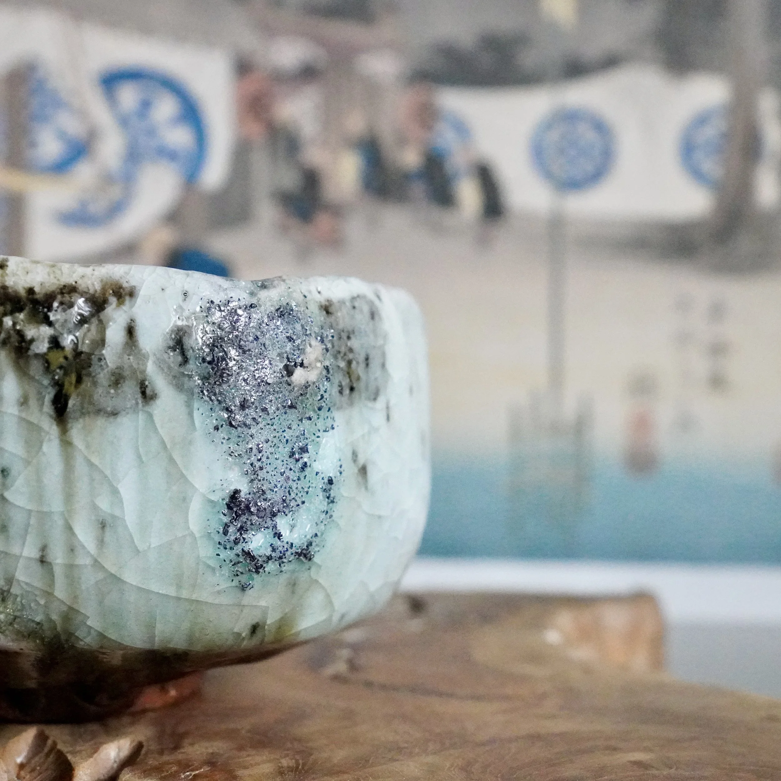 Deguchi Eiji chawan, close-up of a pale crackled glaze with teal, dark brown, and sparkling blue-grey mineral inclusions.