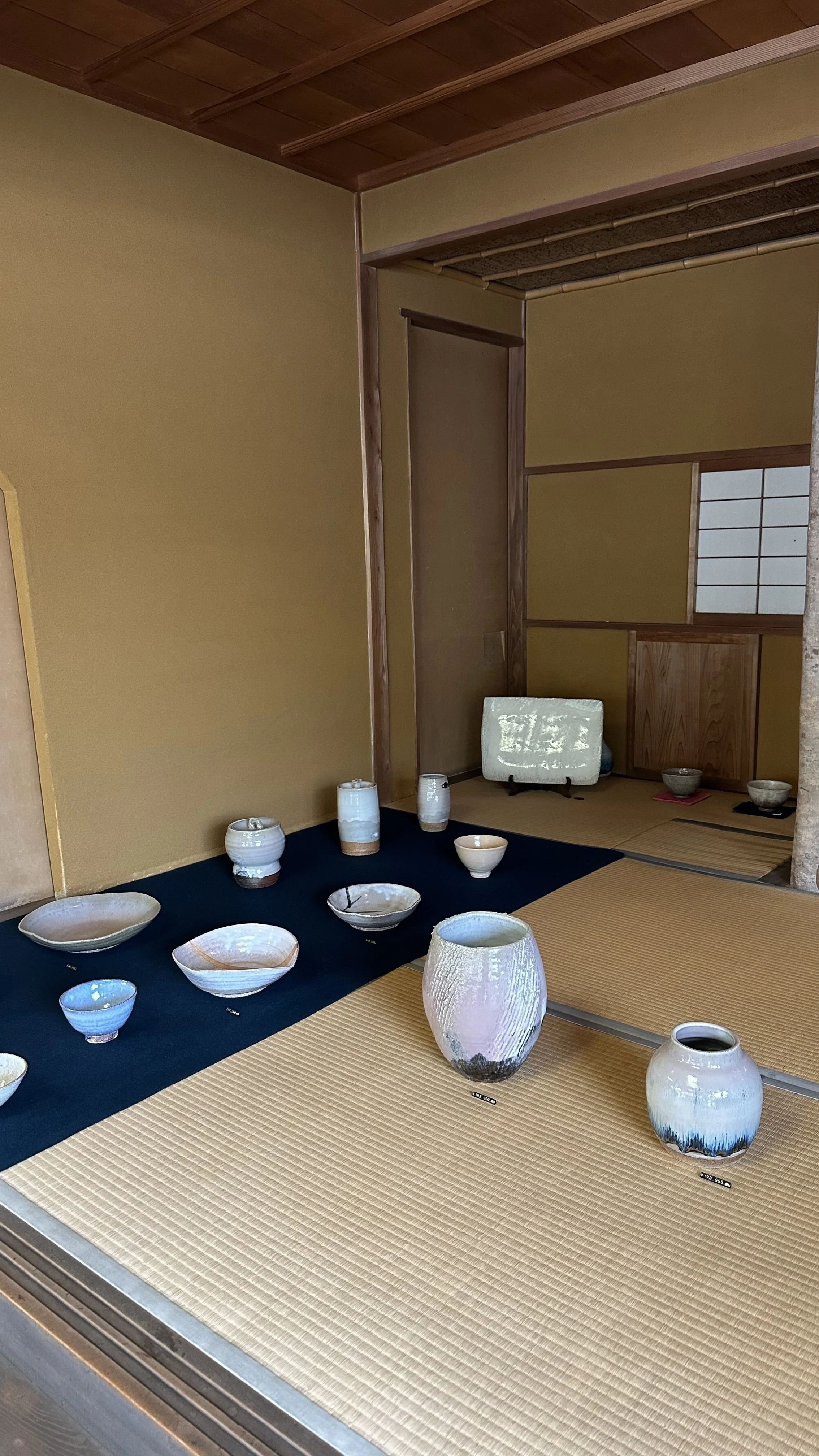 Collection of vintage Hagi-yaki ceramics displayed on tatami mats, including chawan tea bowls in blue and cream glazes, small bowls, a yunomi cup, and two textured vases, photographed at a Japanese studio pottery