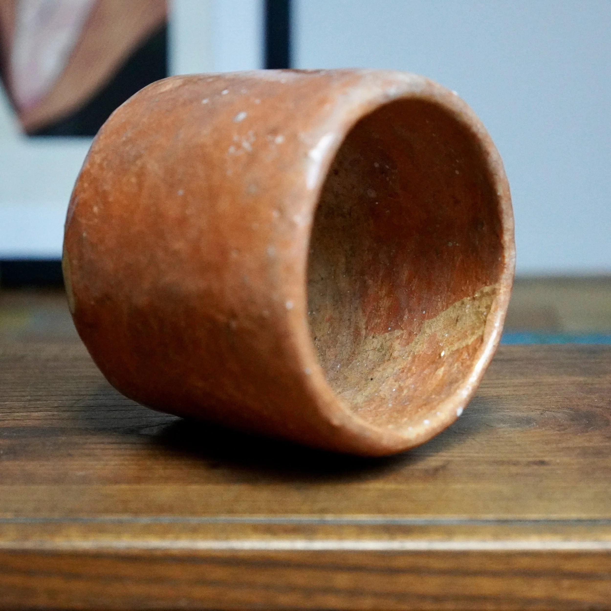 Terracotta-colored tsutsu chawan by Hioki Nanshū kiln, lying on a wooden table, with cream marks and textured surface.