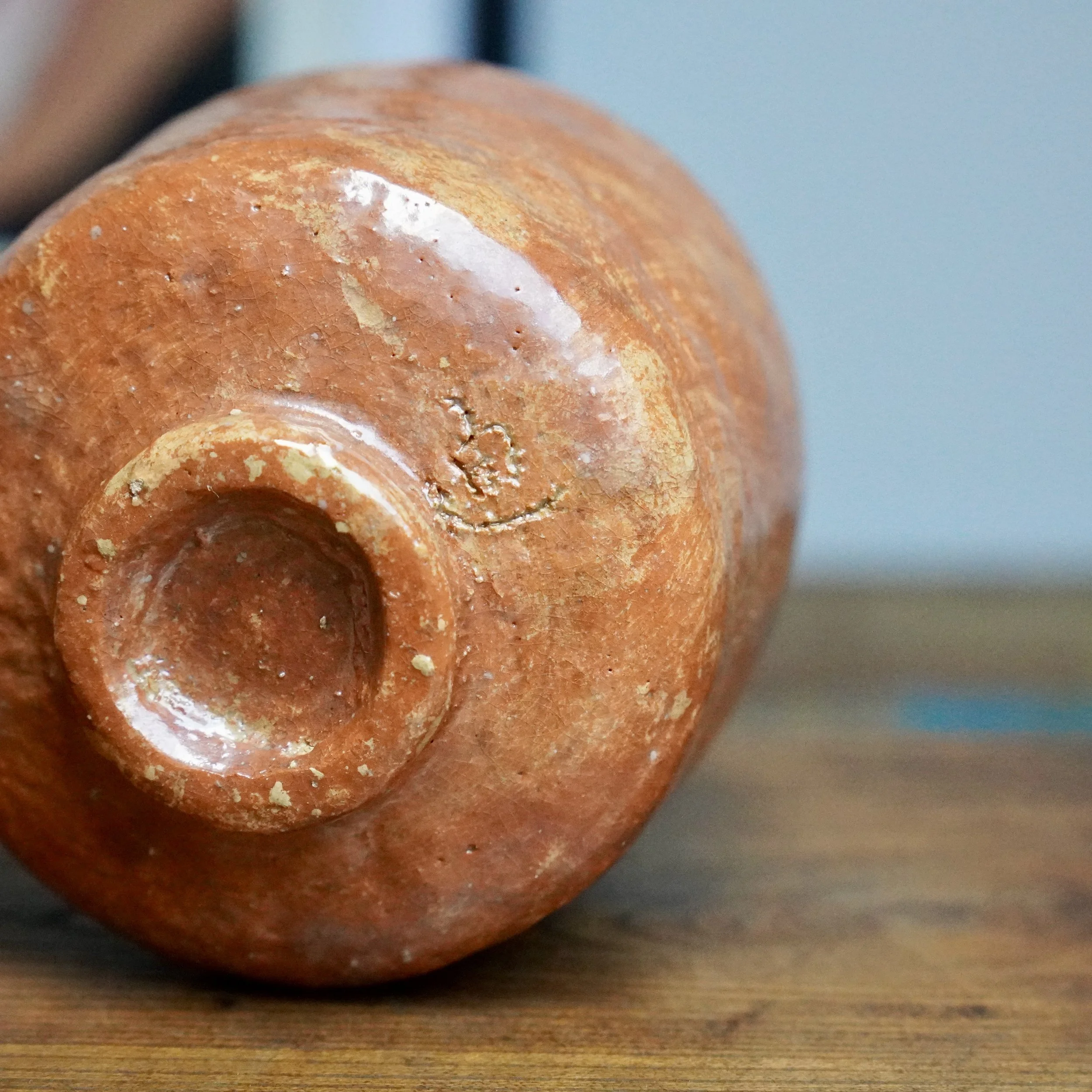 Red-brown tsutsu chawan turned on its side, showing the small foot and an impressed mark. The textured surface has a crackled glaze and glossy white highlights.