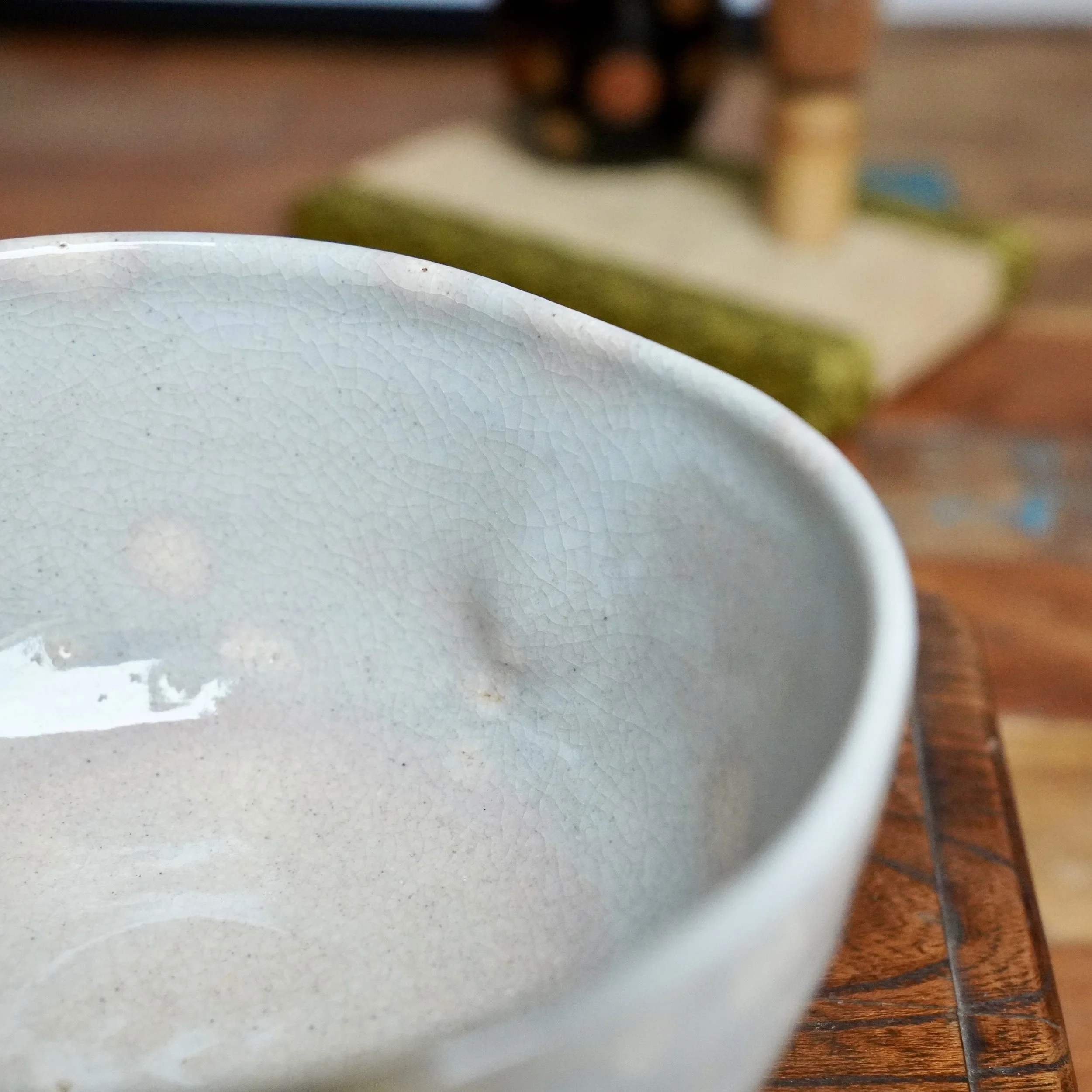 Izushi ware chawan by Nagasawa Minoru, interior view of a grey-blue crackled glaze with a pink blush, resting on a wooden surface.