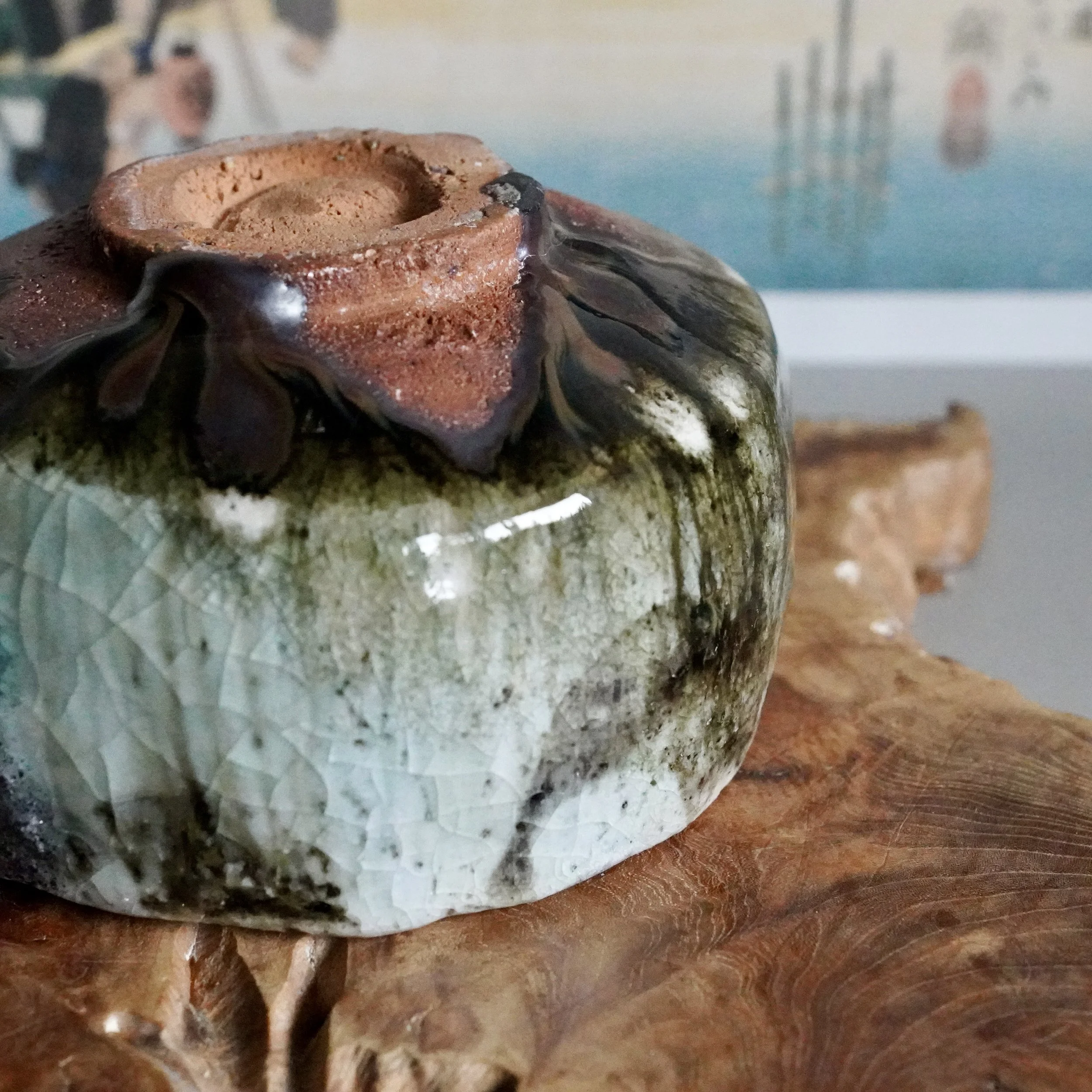 Deguchi Eiji's chawan, showing crackled pale green and dark mottled glaze, with a rough reddish-brown rim, resting on textured wood.