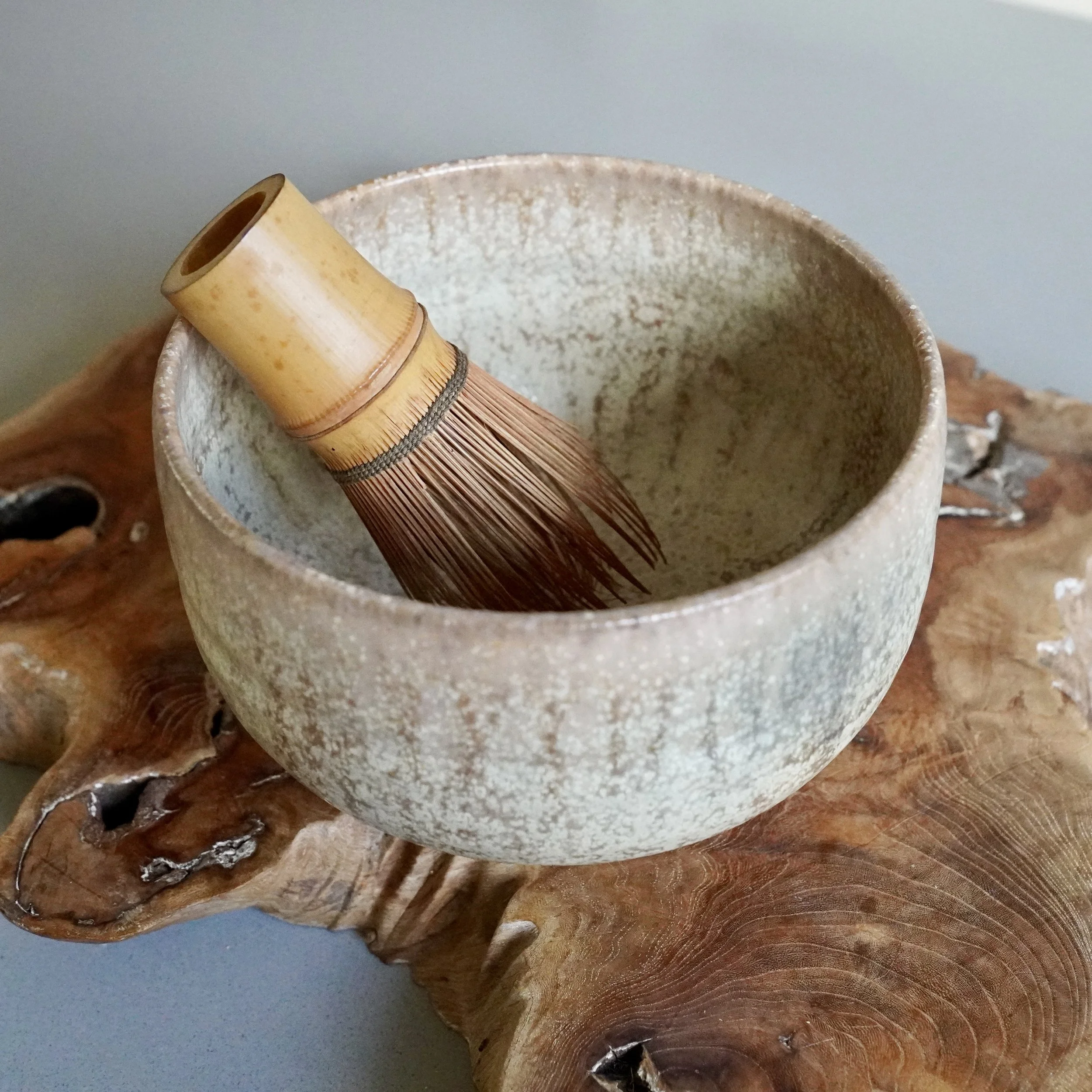 A vintage Hagi-yaki chawan matcha bowl with a pale crackle glaze, shown with a bamboo matcha whisk and its original wooden tomobako box on a natural wood surface.