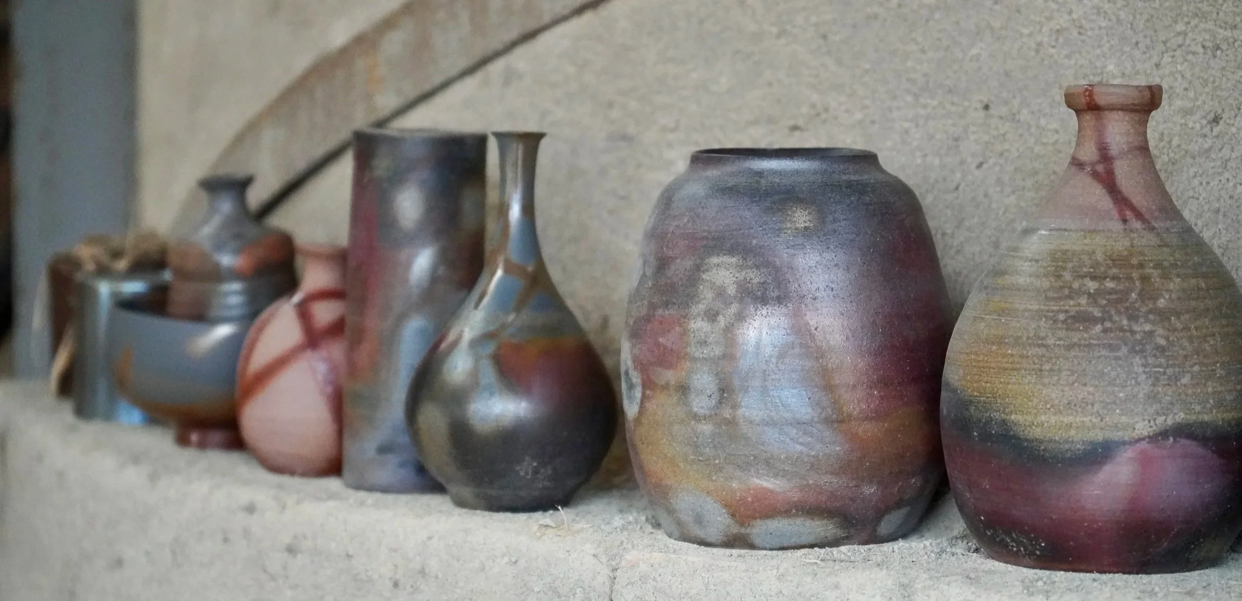 Bizen-yaki ceramics lined up on the edge of a noborigama kiln in Imbe Okayama Japan, showing sangiri grey-purple hiiro red and goma brown kiln effects side by side