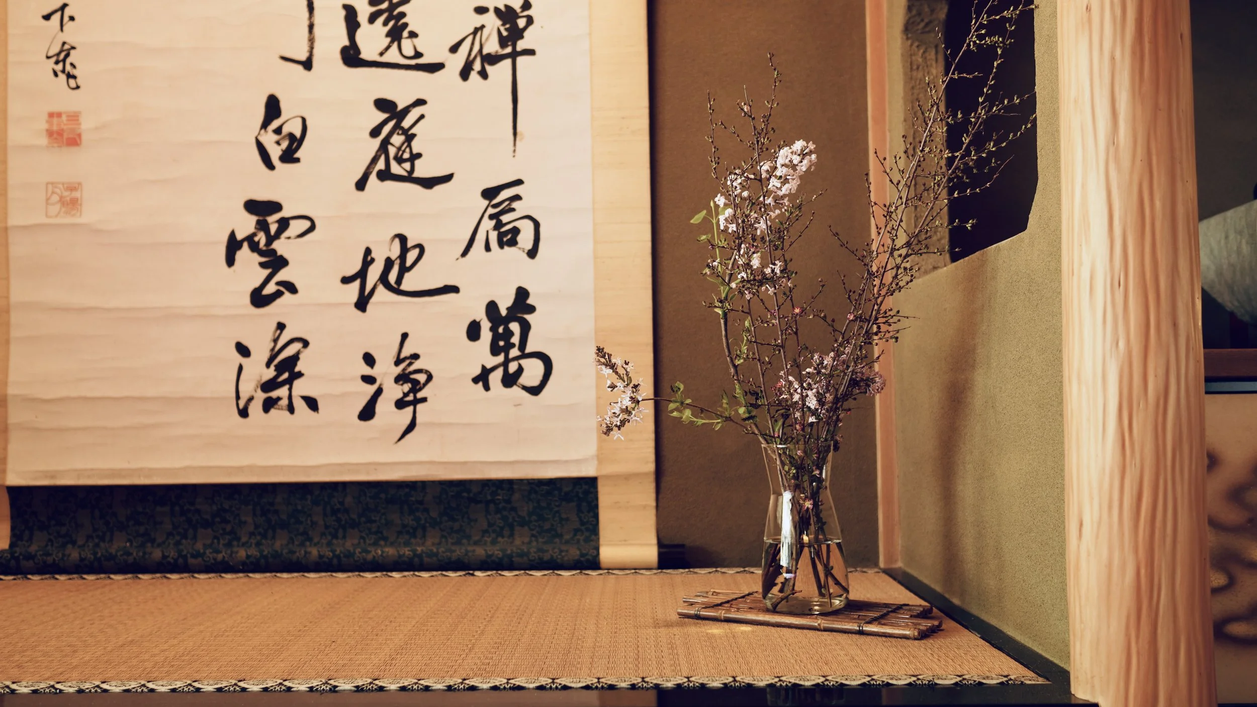 Japanese tokonoma alcove with a large Zen calligraphy kakejiku and a glass vase holding cherry blossom branches on a tatami floor. Tea ceremony room at a Zen temple near Maibara, Shiga Prefecture.