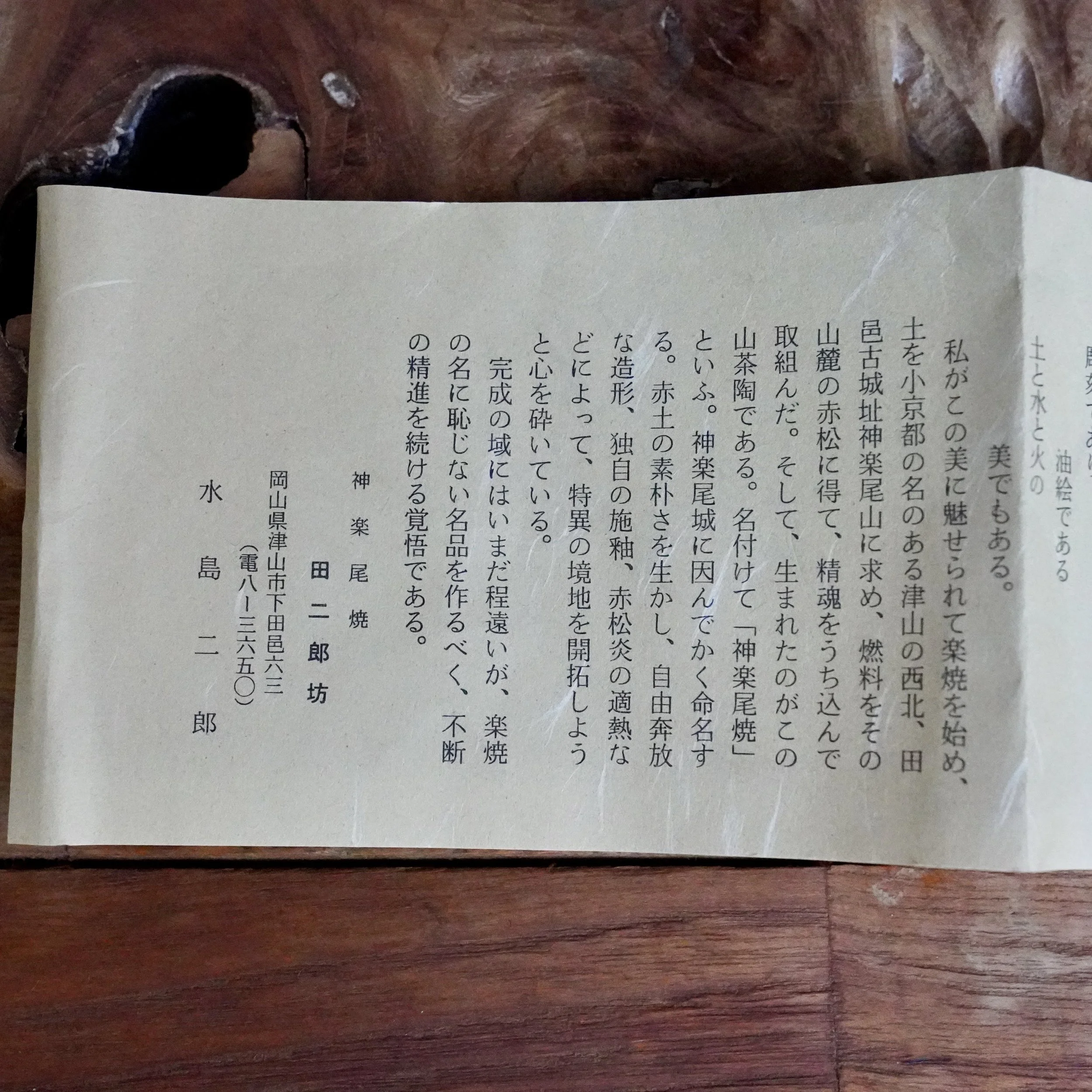 Handwritten Japanese shiori by Mizushima Jirō for a Kagurao-yaki chawan, with vertical script on light paper, resting on a dark wood surface.