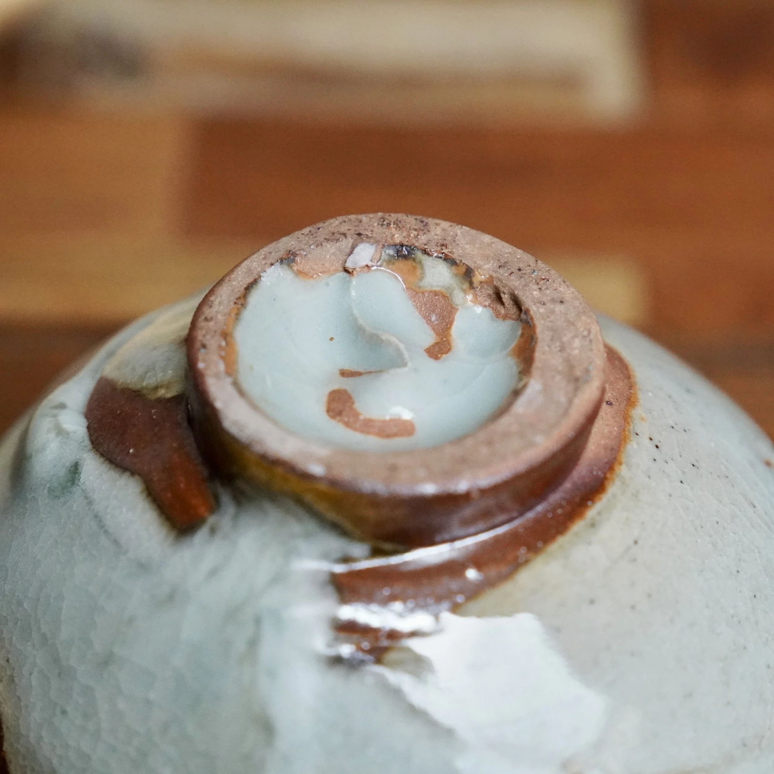 Sansōan chawan, close-up of unglazed, reddish-brown foot with pale blue-grey crackle and rust-brown glaze flow featuring ochre streaks.