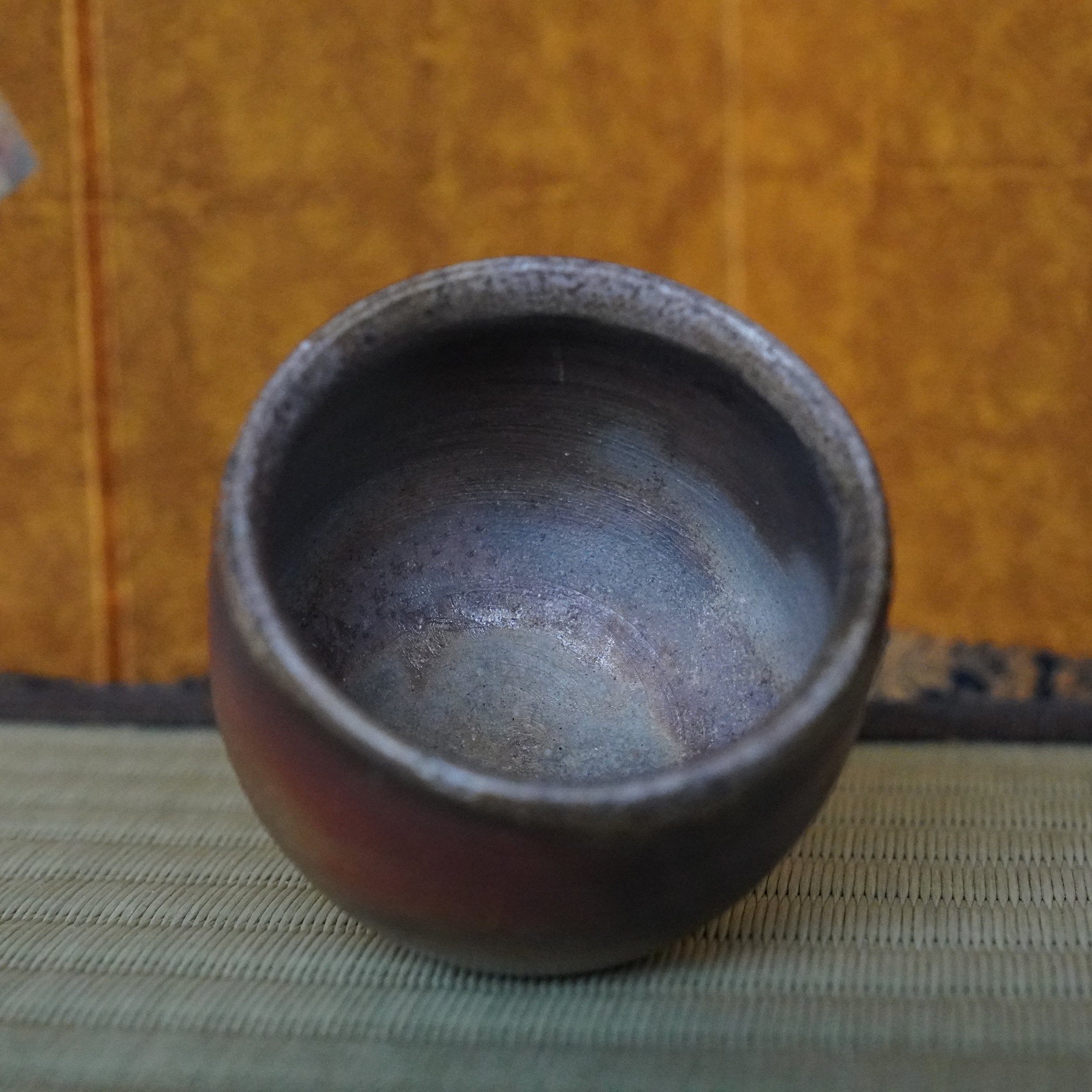 Handcrafted guinomi by Yamamoto Sōshū, featuring an uneven dark rim and interior with textured blue-grey tones. Reddish-brown hidasuki marks are visible on the lower exterior.