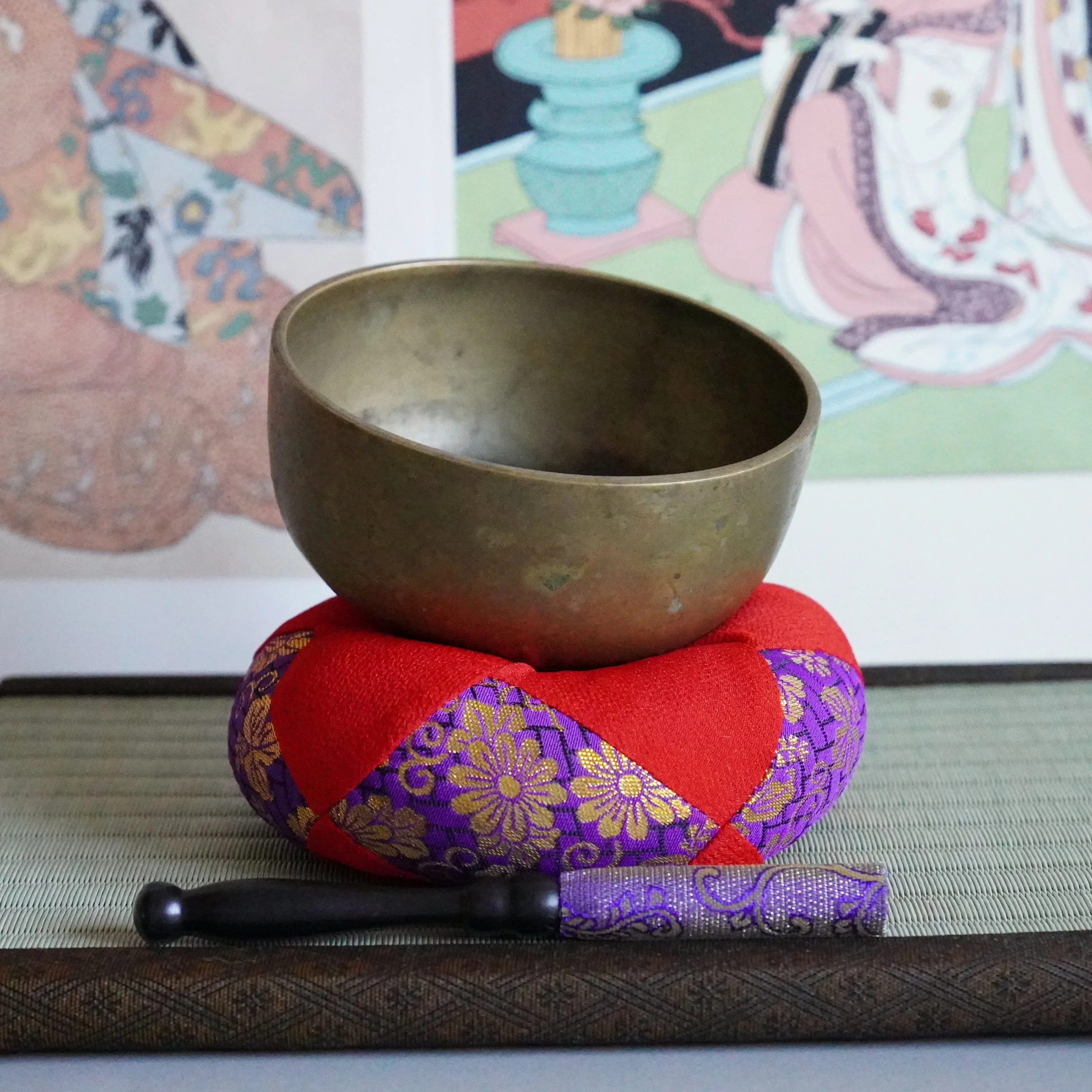 Bronze orin singing bowl on cushion with striker, angled view, tatami mat