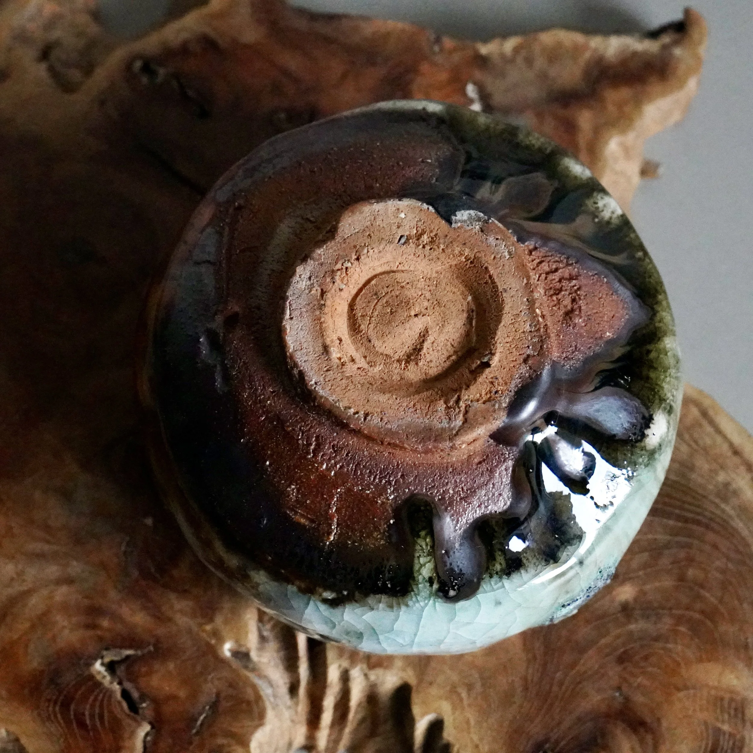 Underside of a wood-fired chawan by Deguchi Eiji, showing a rustic reddish-brown unglazed foot, dark brown and reddish glaze, and a crackled light blue-green base.