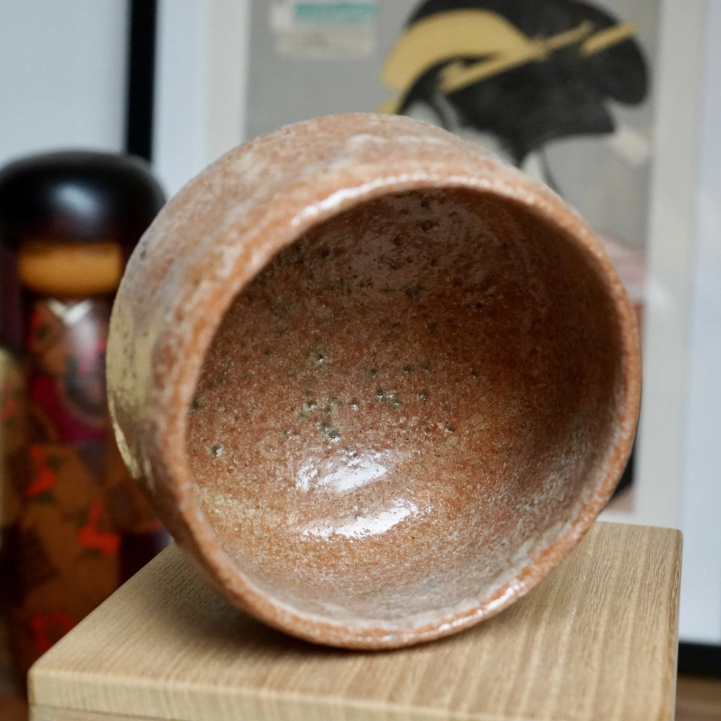 Sawada Hiroyuki's Aka-raku chawan, a rugged reddish-brown tea bowl with a speckled surface, glossy patches, and a pale white glaze drip.
