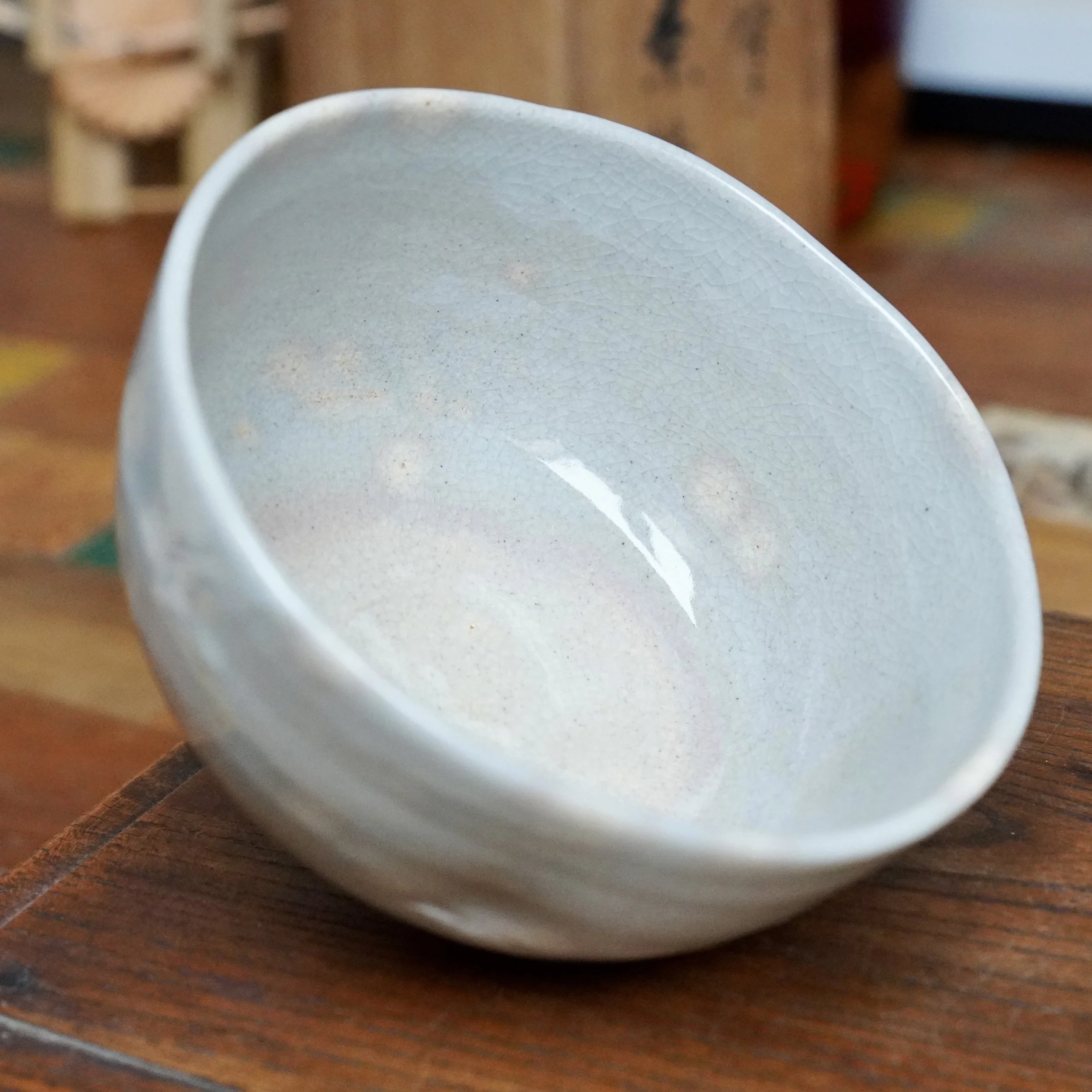 Nagasawa Minoru, Izushi-gama chawan with a soft grey-blue crackled glaze and pink blush visible in the interior, on a wooden surface.