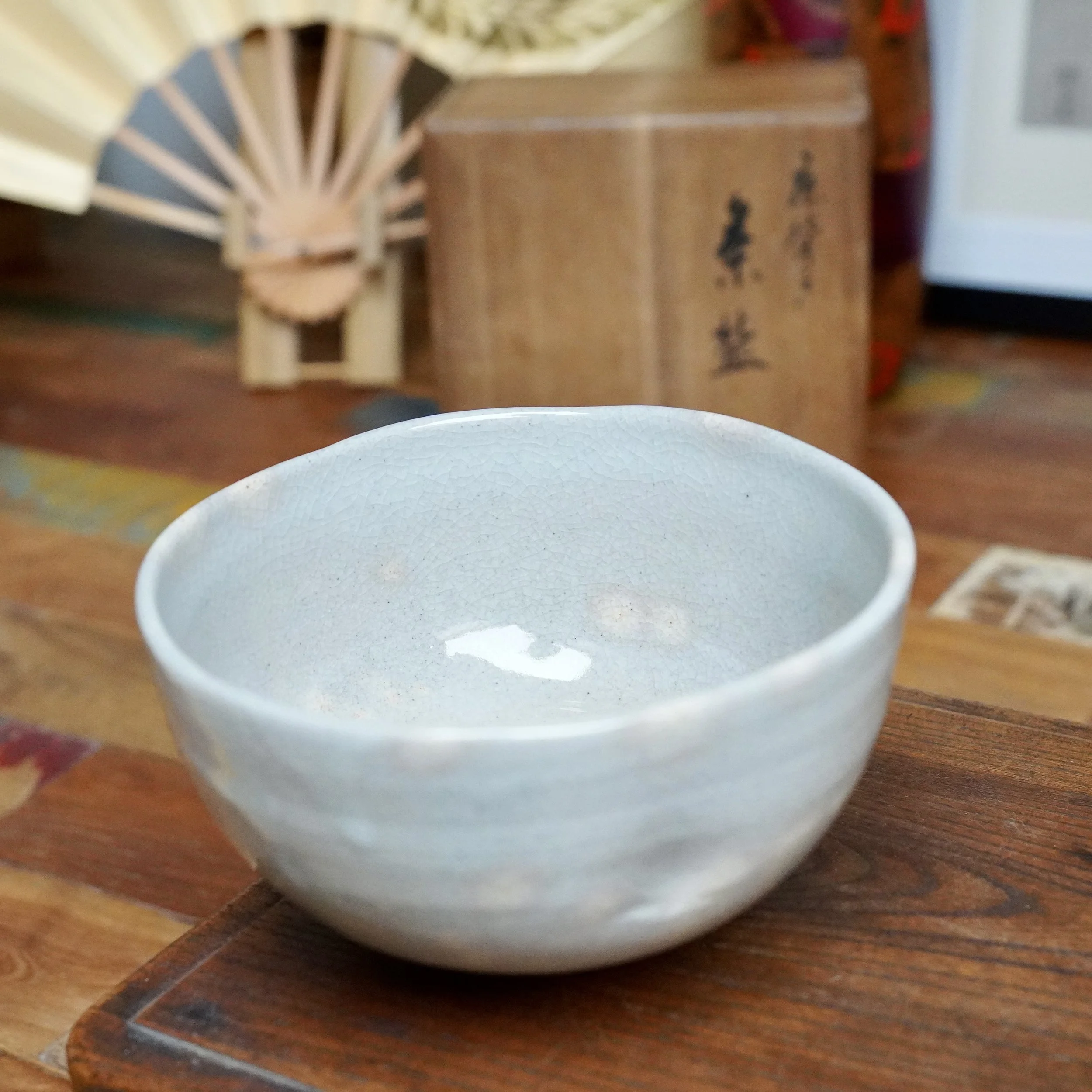 Crackle-glazed grey-blue chawan by Nagasawa Minoru, with pink blushes showing through, resting on dark wood.