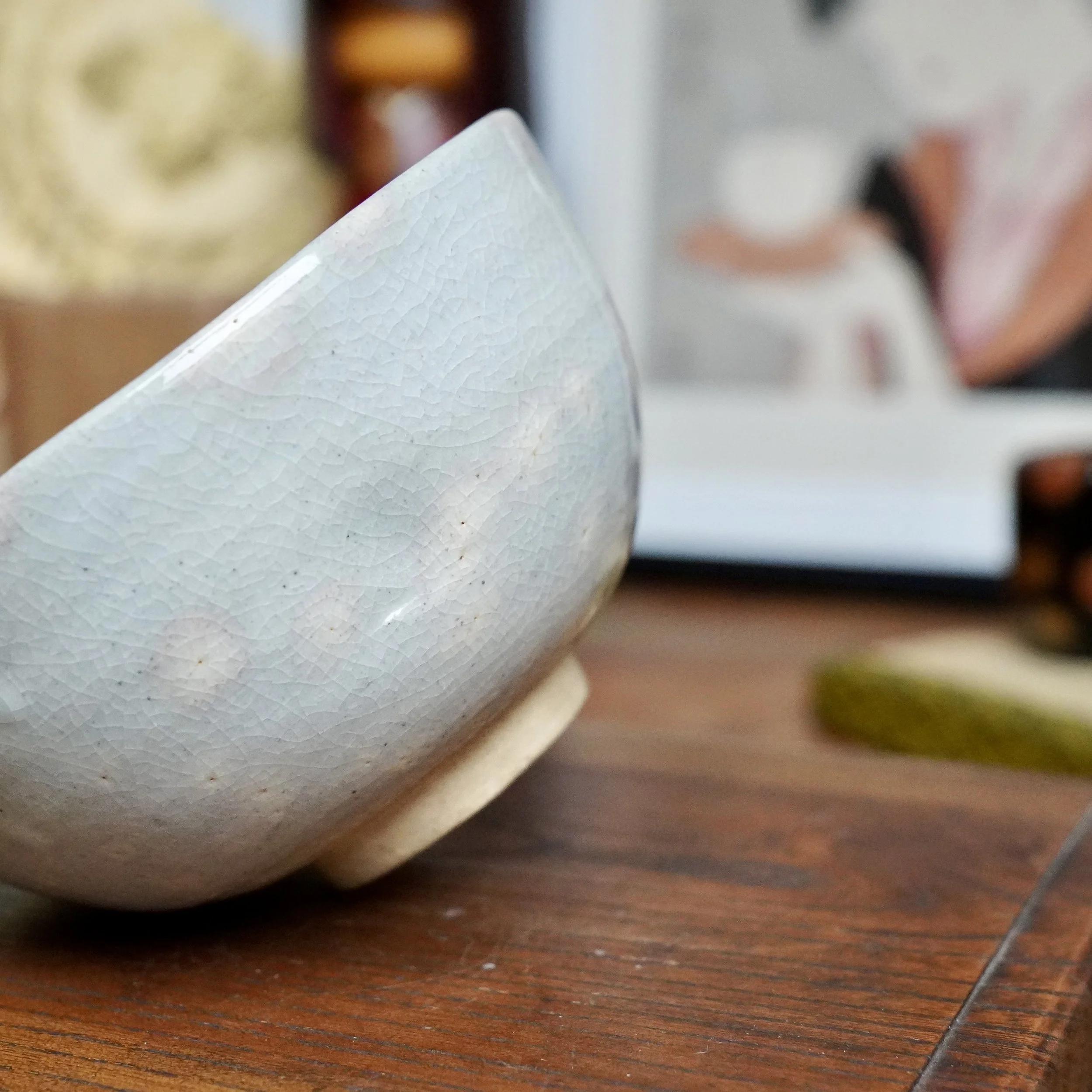 Izushi ware chawan by Nagasawa Minoru, showing its crackled grey-blue glaze with faint pink blush, unglazed base, and a wooden surface from a low angle.