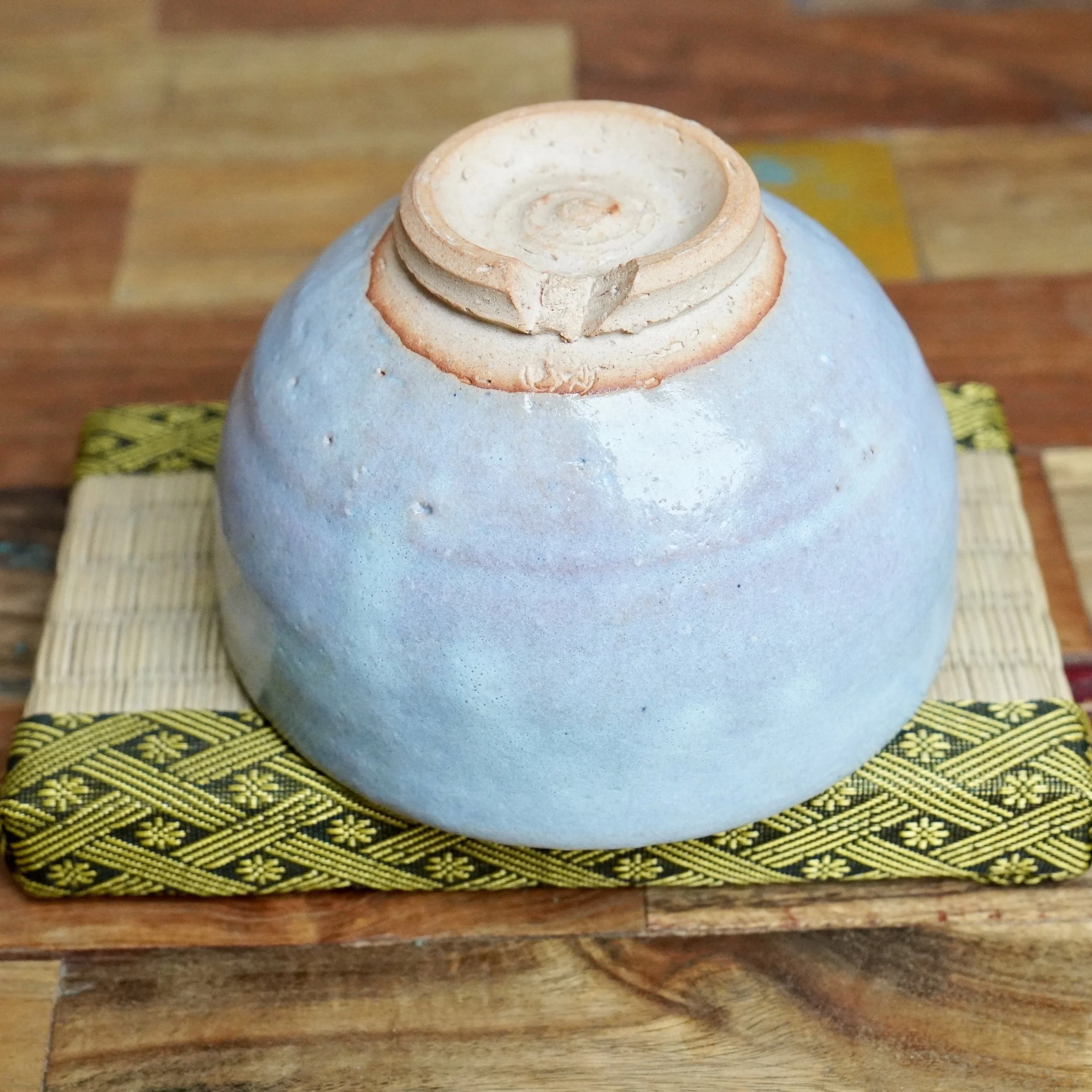 Underside of a light blue-grey glazed Hagi-yaki chawan, revealing its unglazed warikodai foot, with an impressed signature by Moriwaki Fumitada, resting on a woven mat.