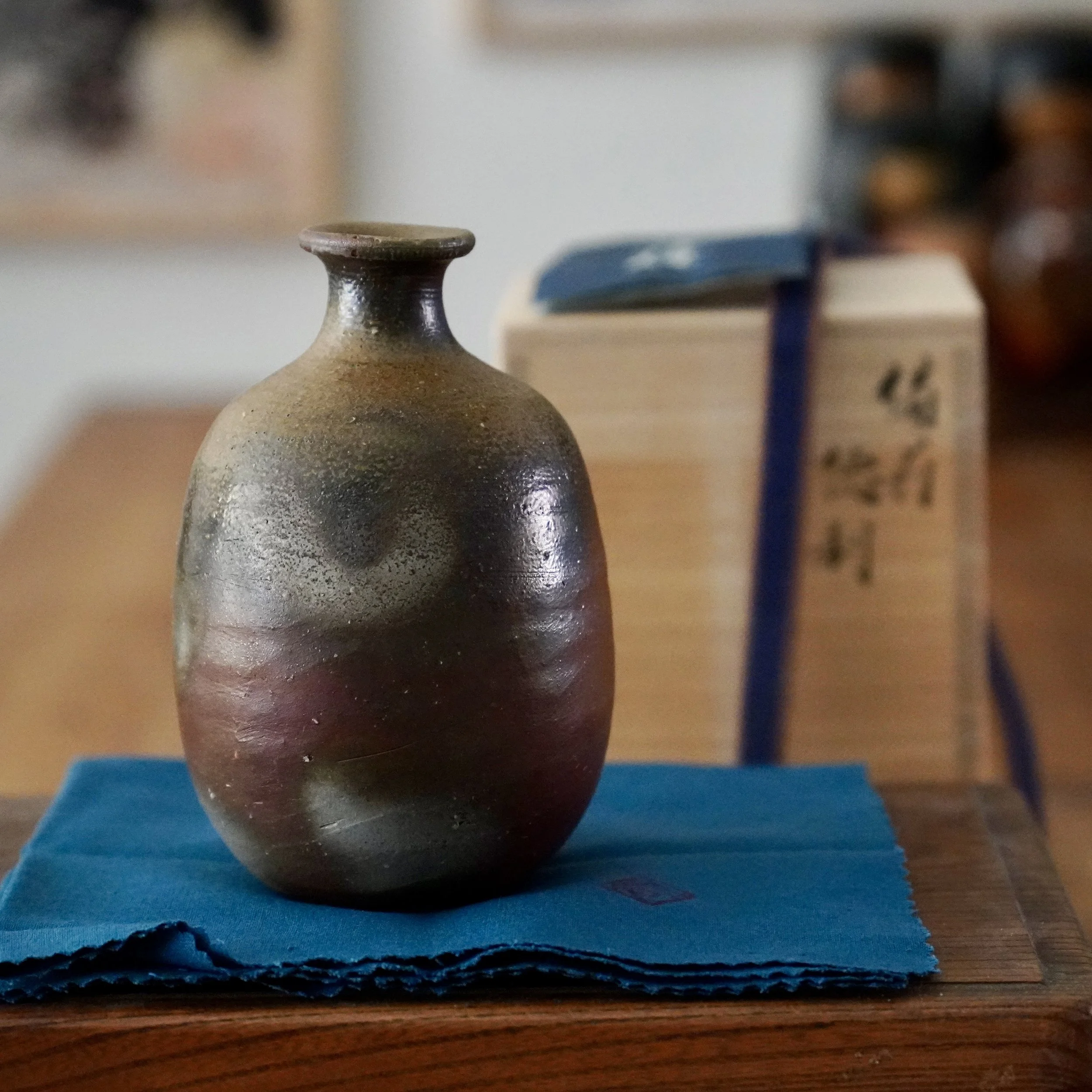 Bizen-yaki tokkuri by Isezaki Sō on its wrapping cloth, front view showing the olive to aubergine ash glaze