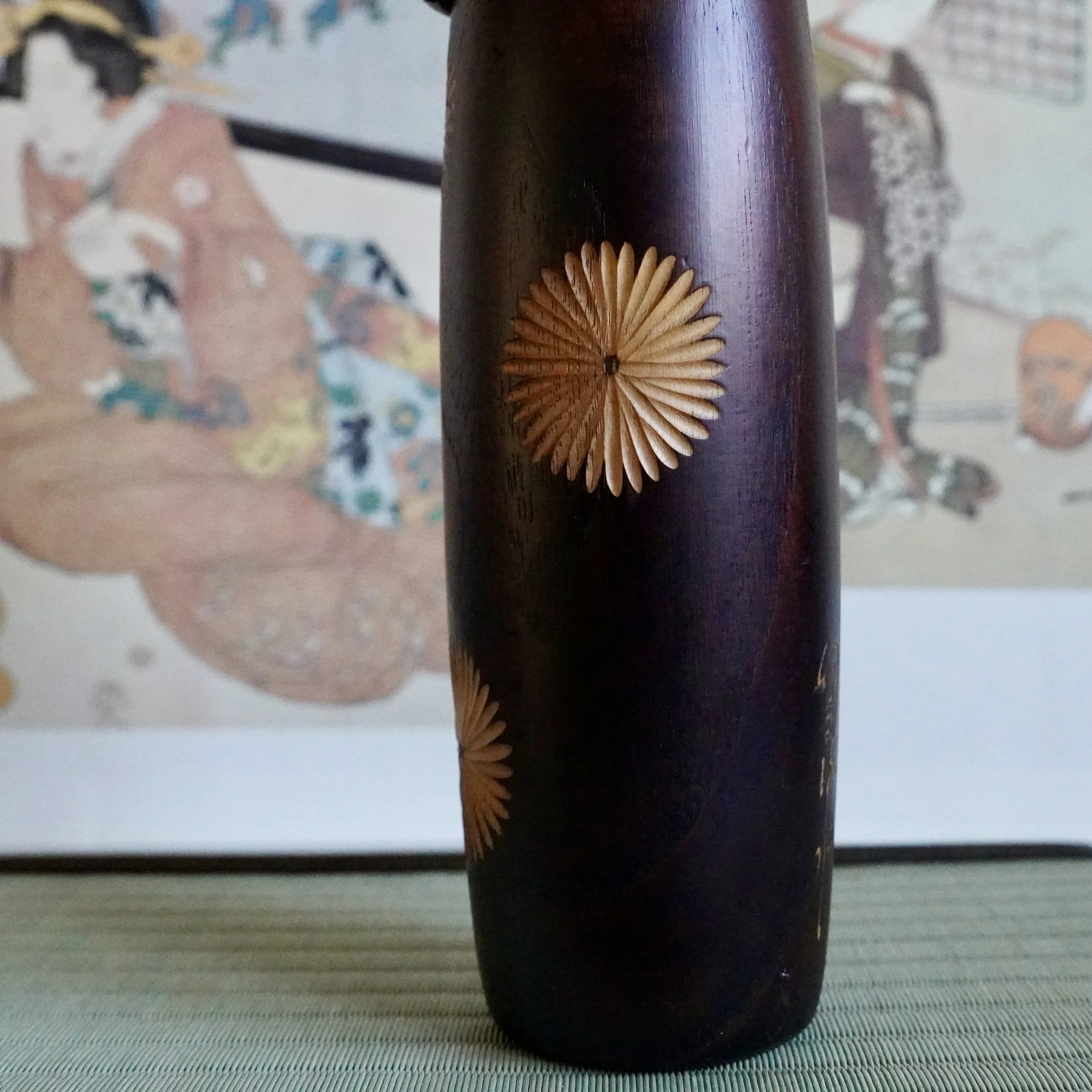 Sosaku kokeshi angle view, single chrysanthemum wood inlay medallion on aubergine stained body