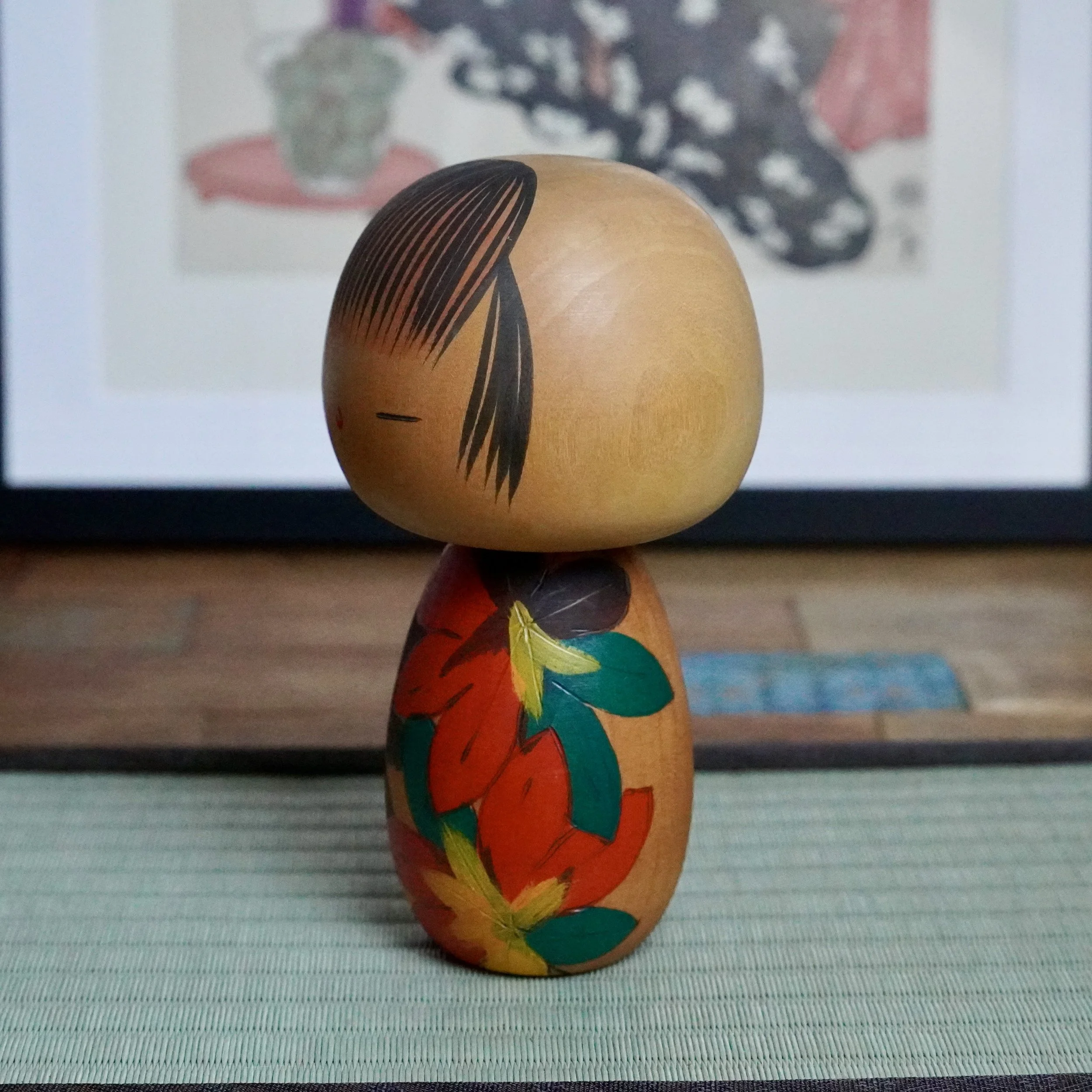 Yuji Kawase kokeshi doll, natural wood head and black hair, body carved with red, dark green, yellow, and near-black momiji leaves.