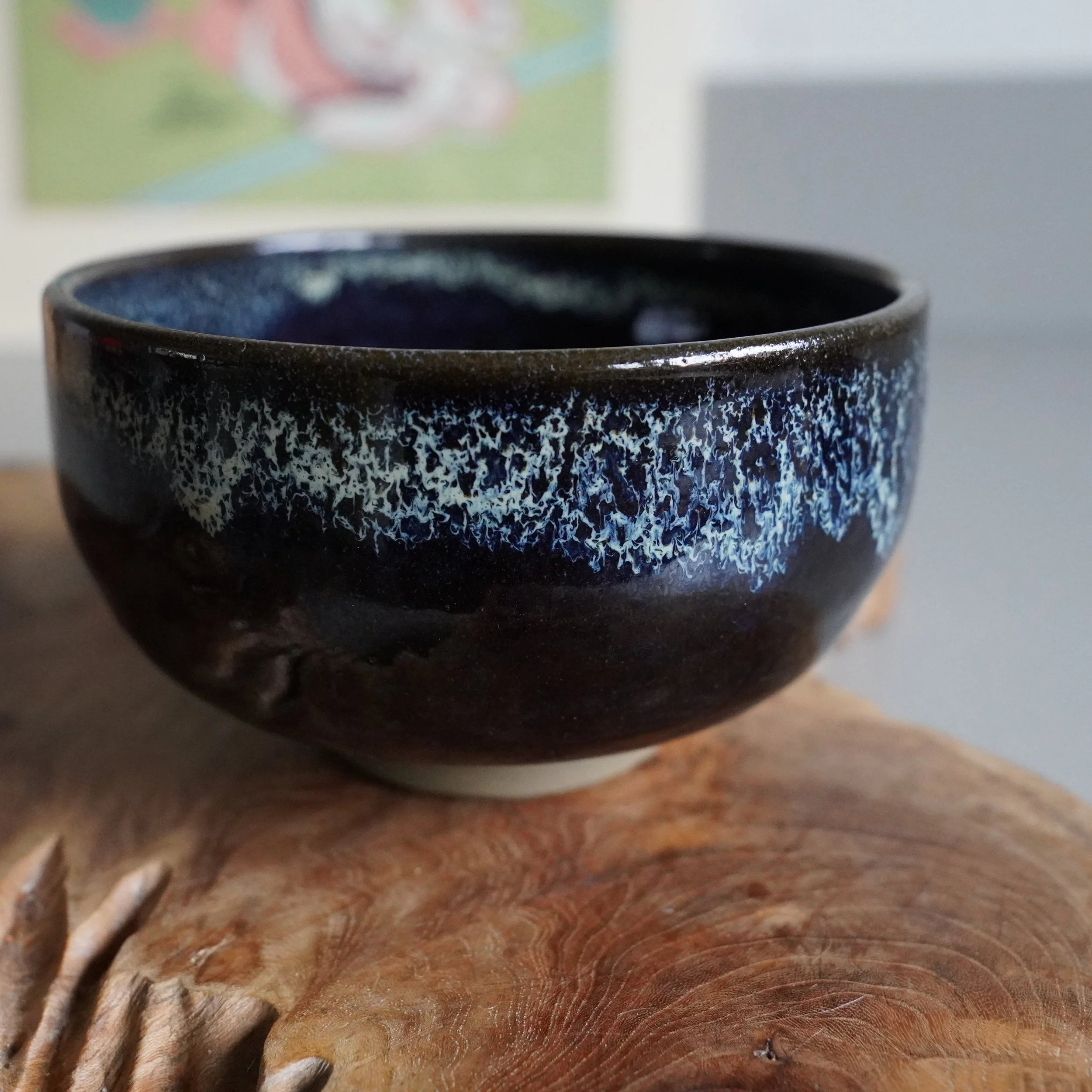Deep brown ceramic matcha bowl with mottled blue-white glaze patterns, by Rokuhō, resting on a textured wooden surface.