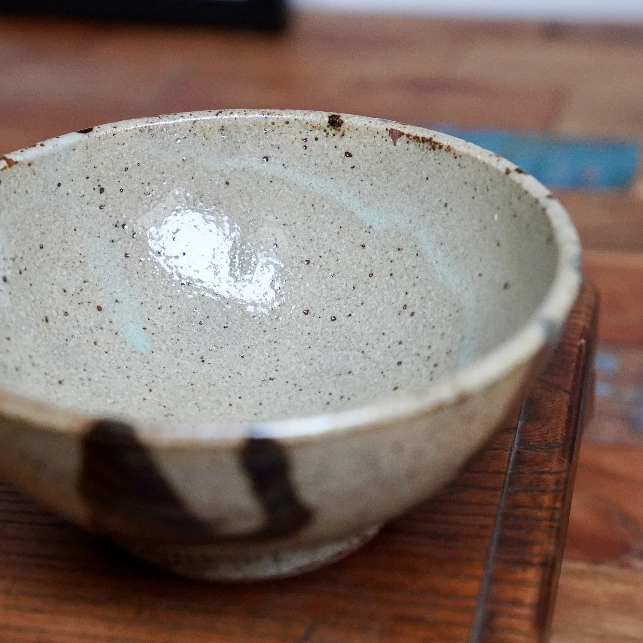 Shallow ceramic bowl from Maruta Nobumasa kiln. Speckled light grey interior glaze with milky white drips, blue accents, and dark brush strokes on exterior.